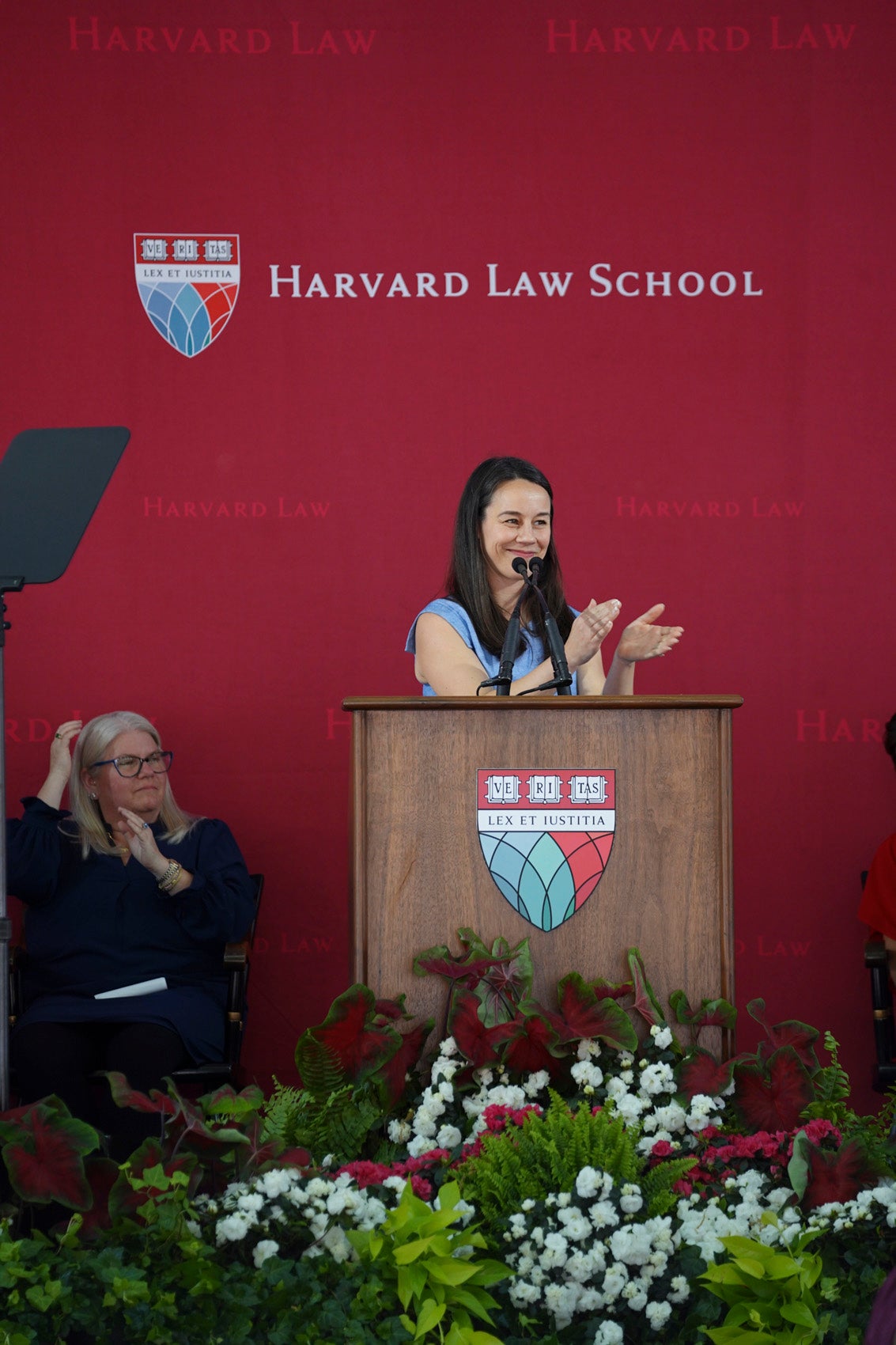 Merry Boak standing behind podium, clapping