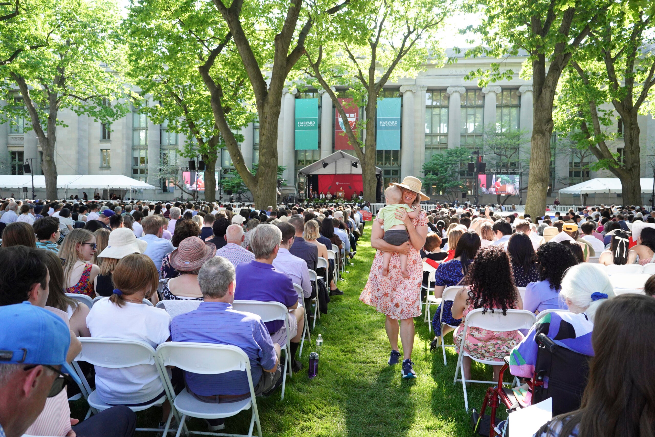 A woman with a child in arms walks between rows of people attending an event