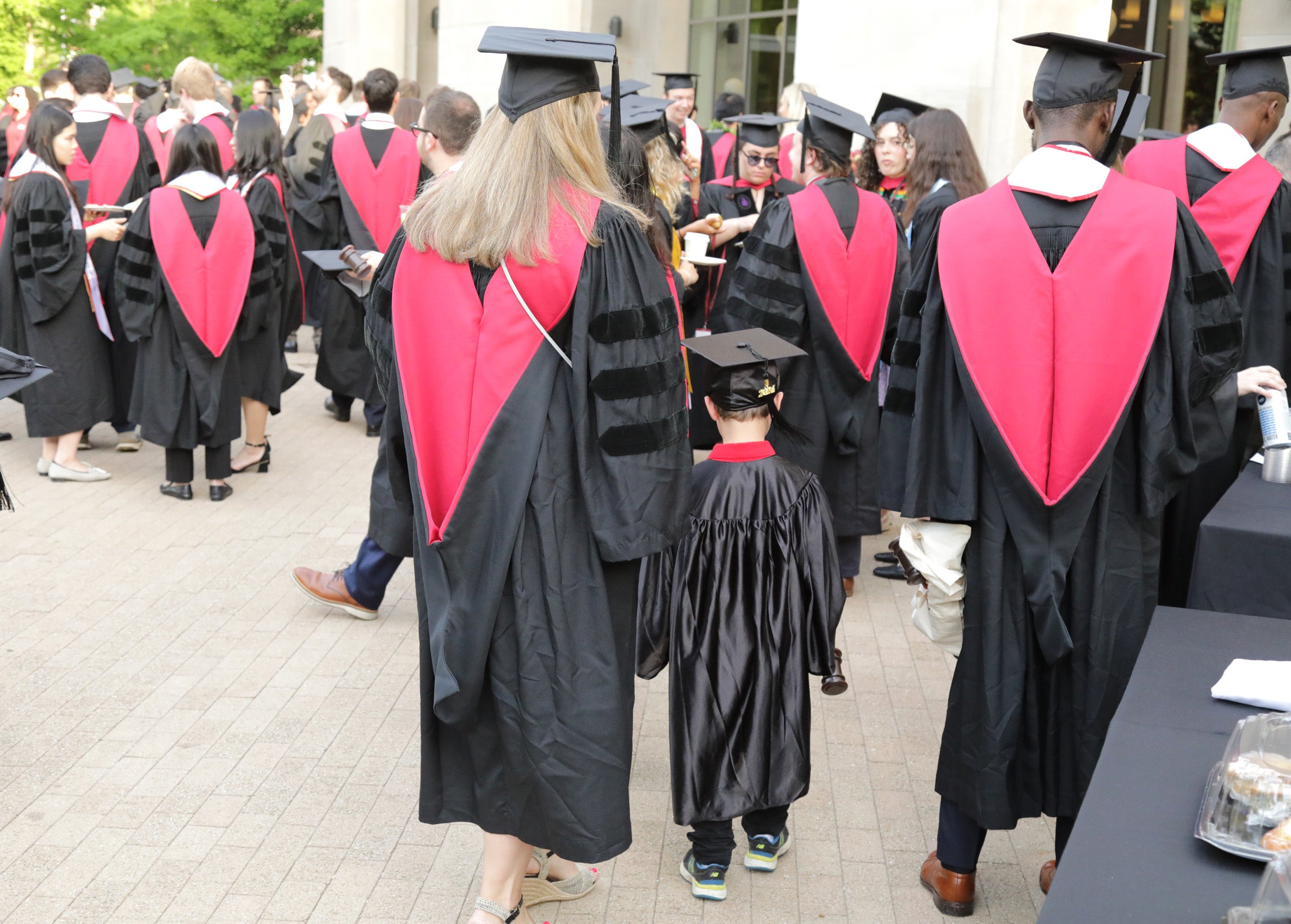 A woman in a cap and gown holding the hand of a young boy in a cap and gown