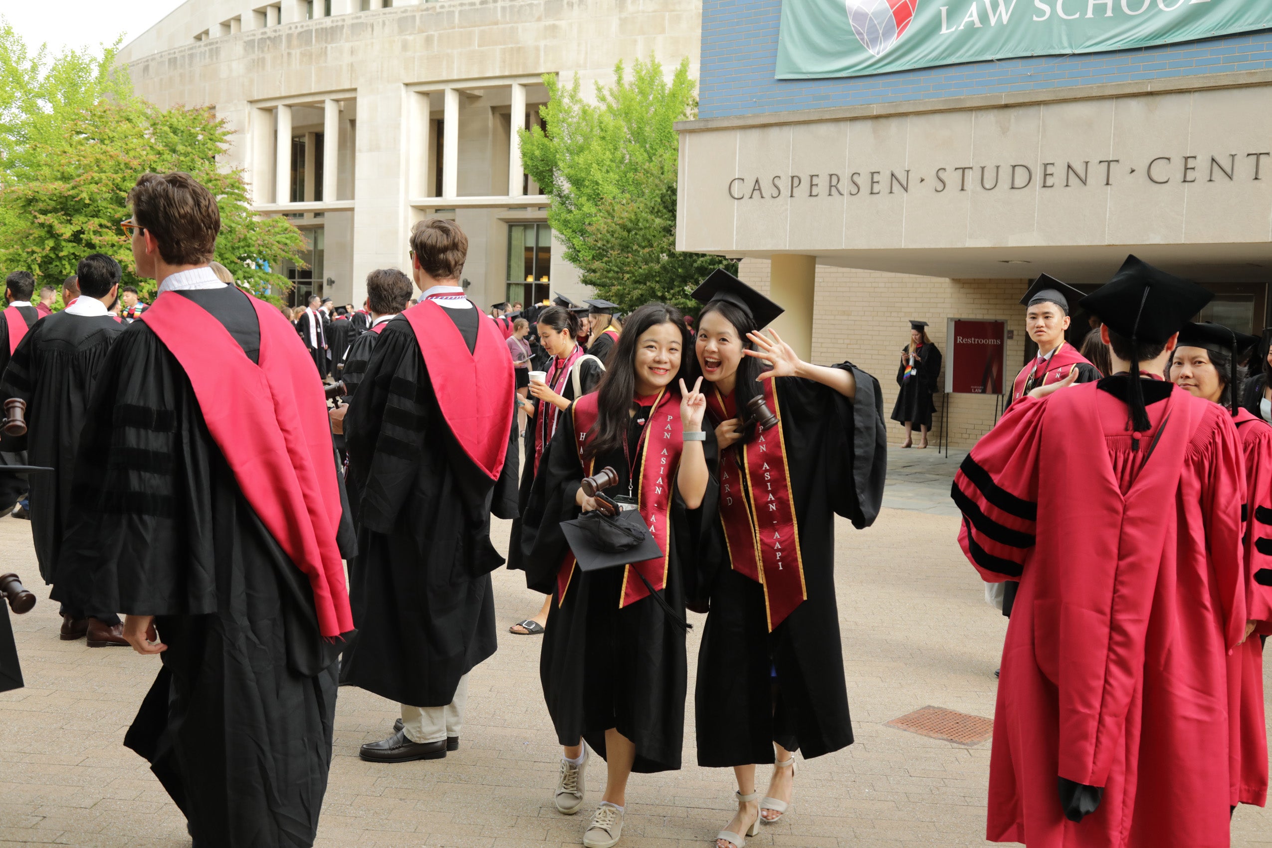Two students smiling and waving among a big group of students in regalia.
