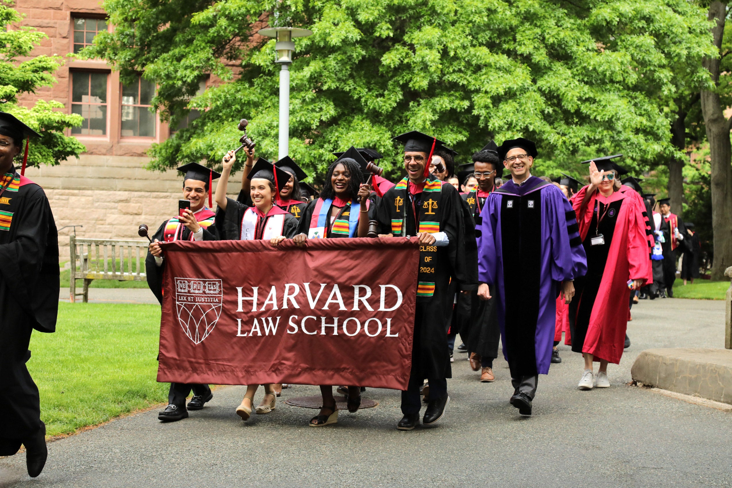A group of students in cap and gown carry a banner that says Harvard Law School through campus