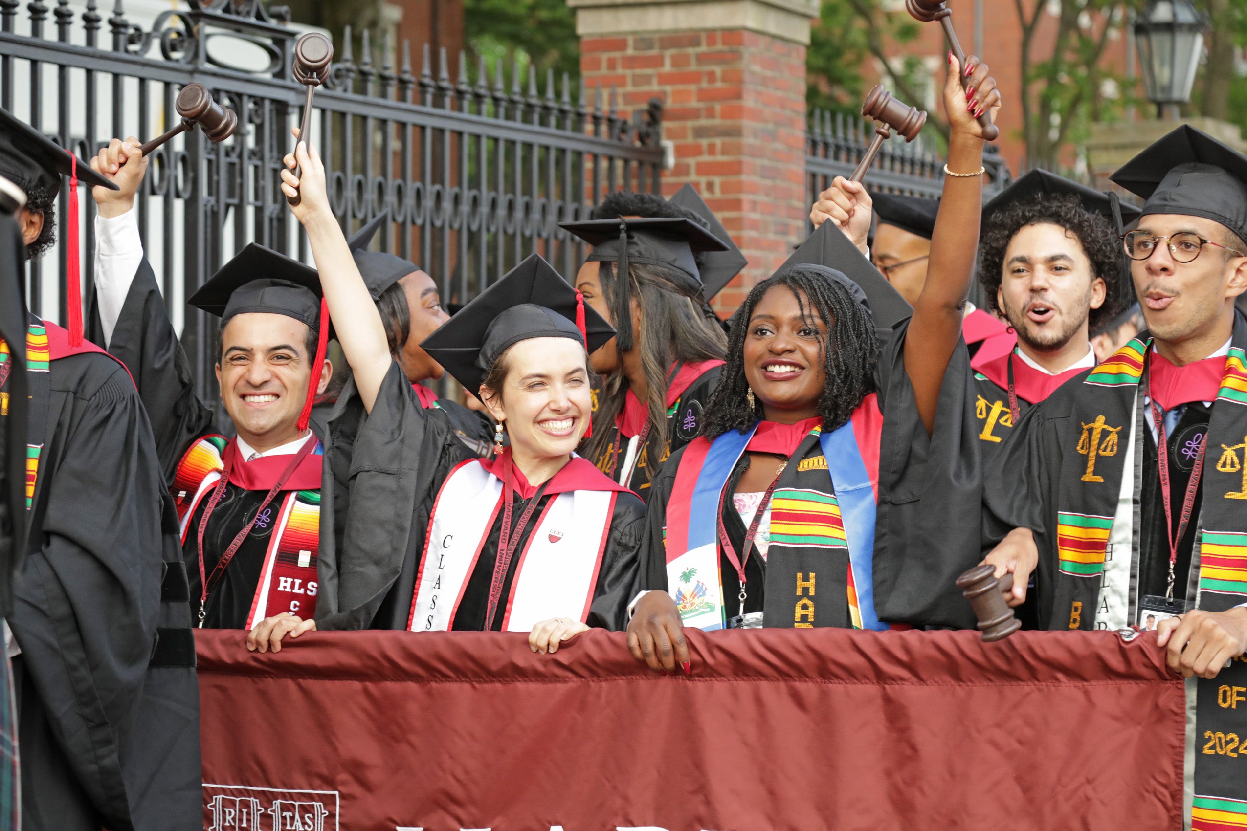 A group of students in cap and gown cheering and holding a banner.
