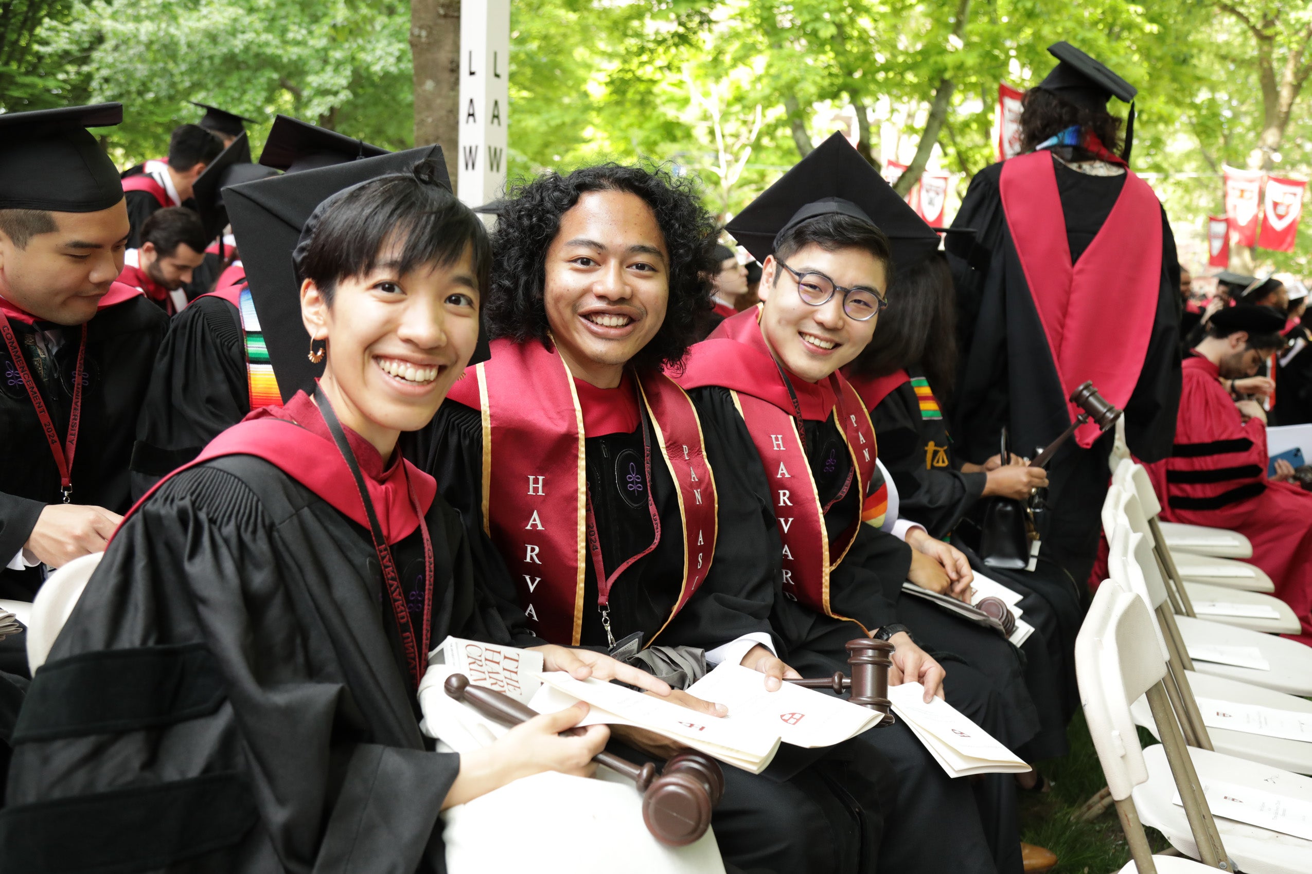 Three graduates seated in Harvard Yard, smiling