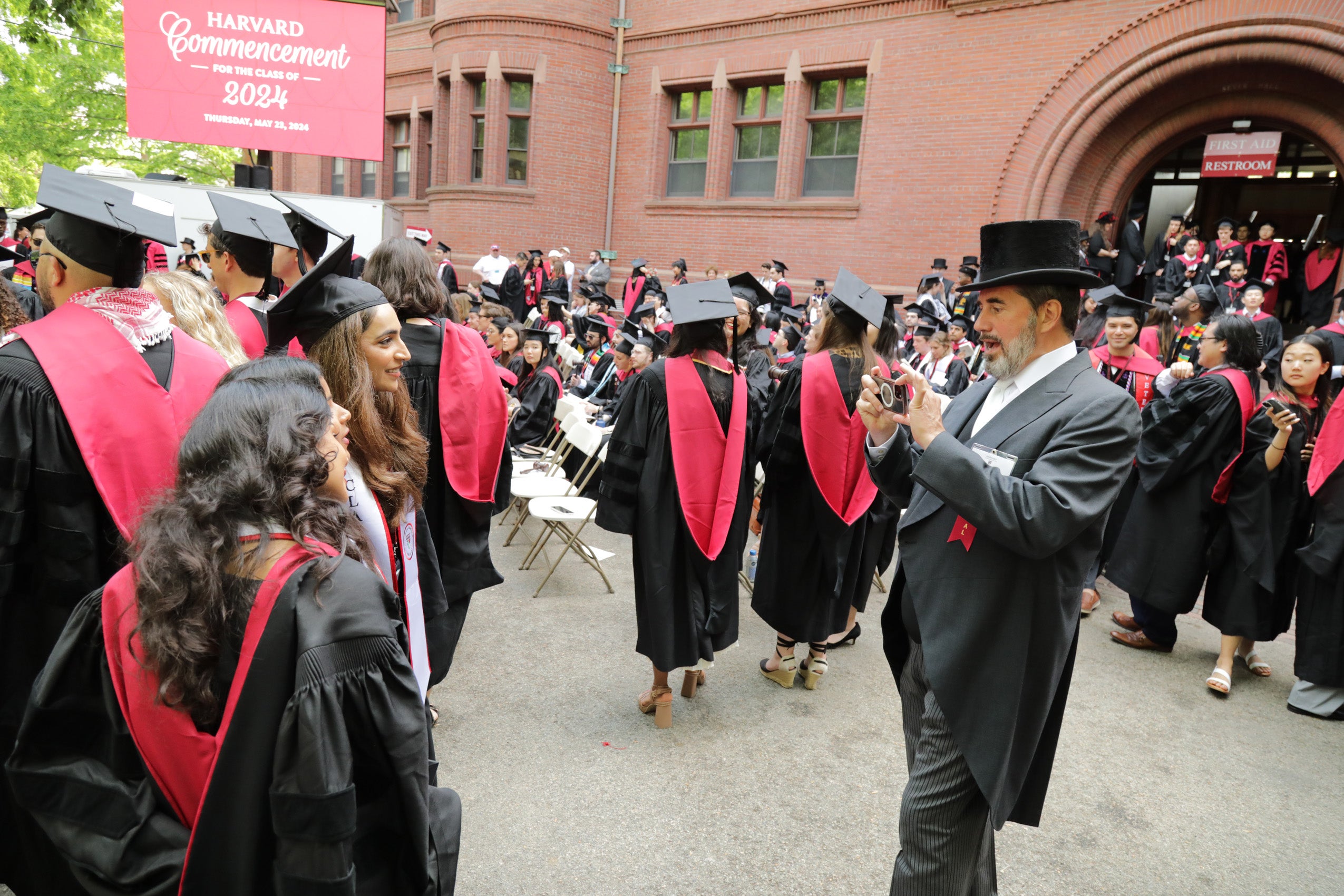 Two graduates having their photo taken in Harvard Yard by a man in a top hat