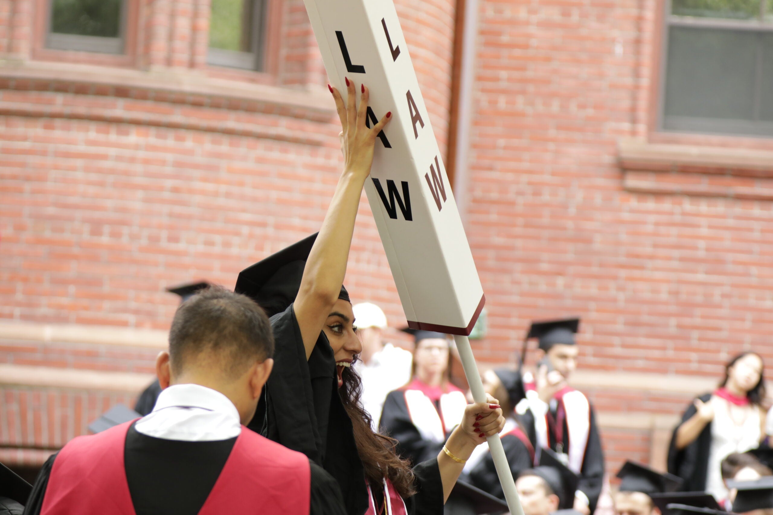 Excited graduating student holding up a LAW pillar