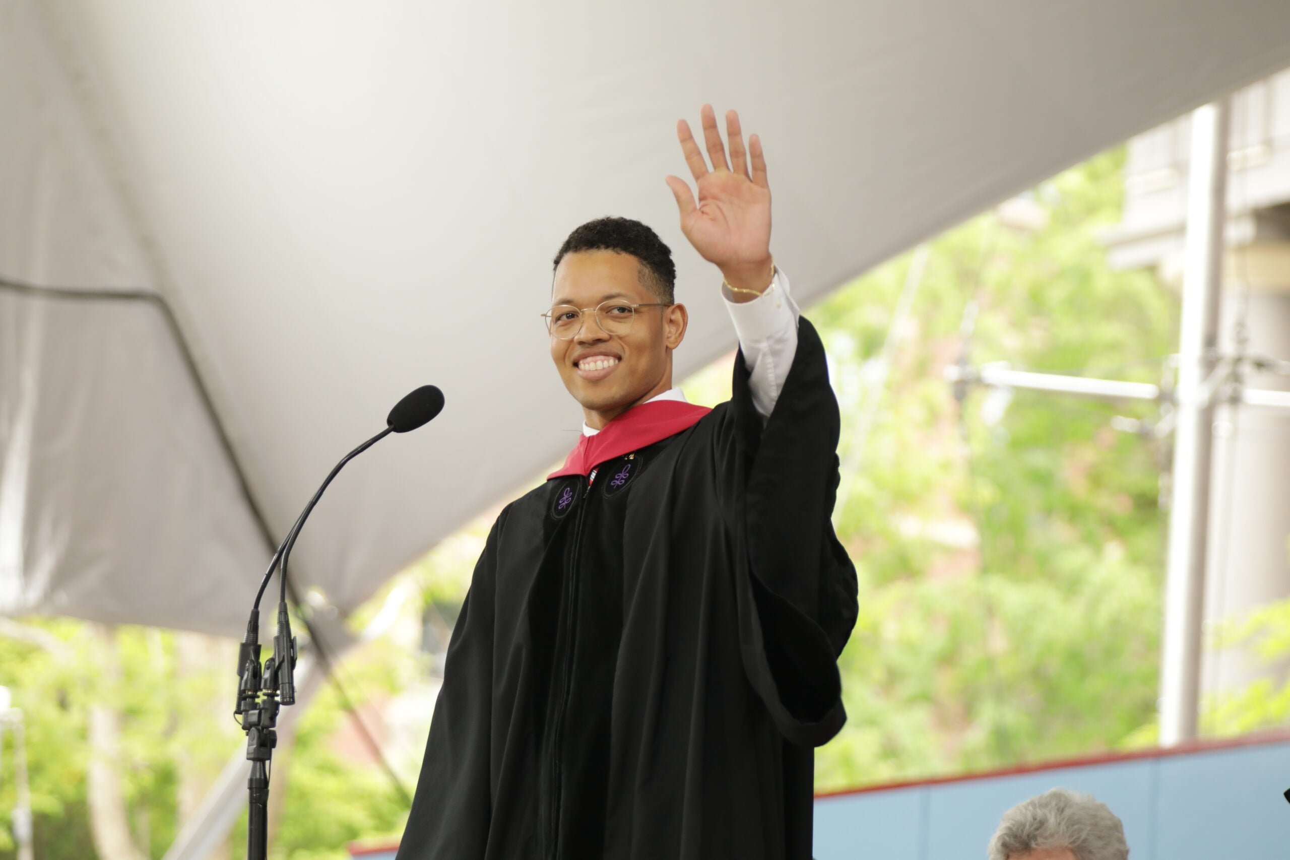 Student in Commencement regalia waving from stage