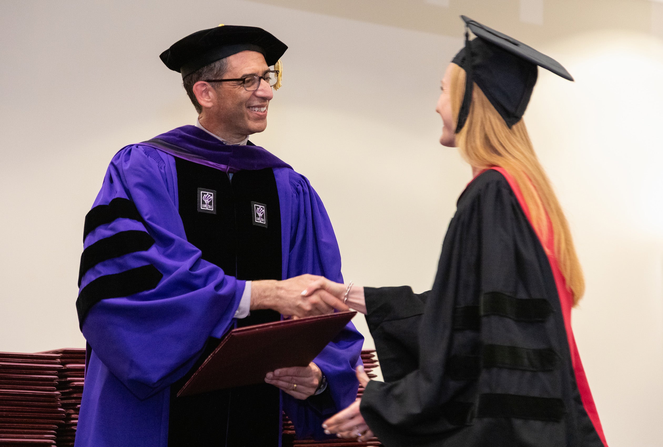 Dean Goldberg shakes the hand of a female graduate and gives her a diploma.