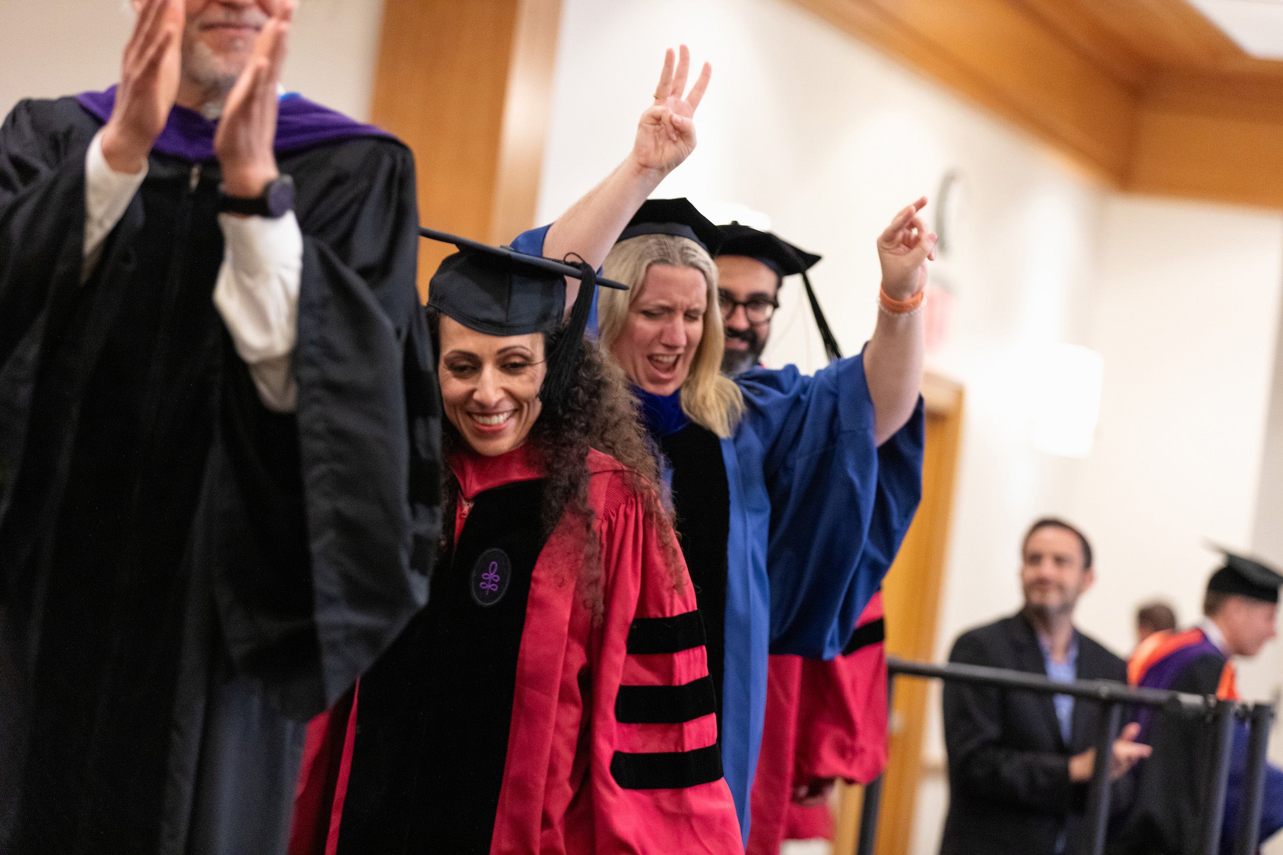 Faculty in cap and gown cross the stage cheering the graduates