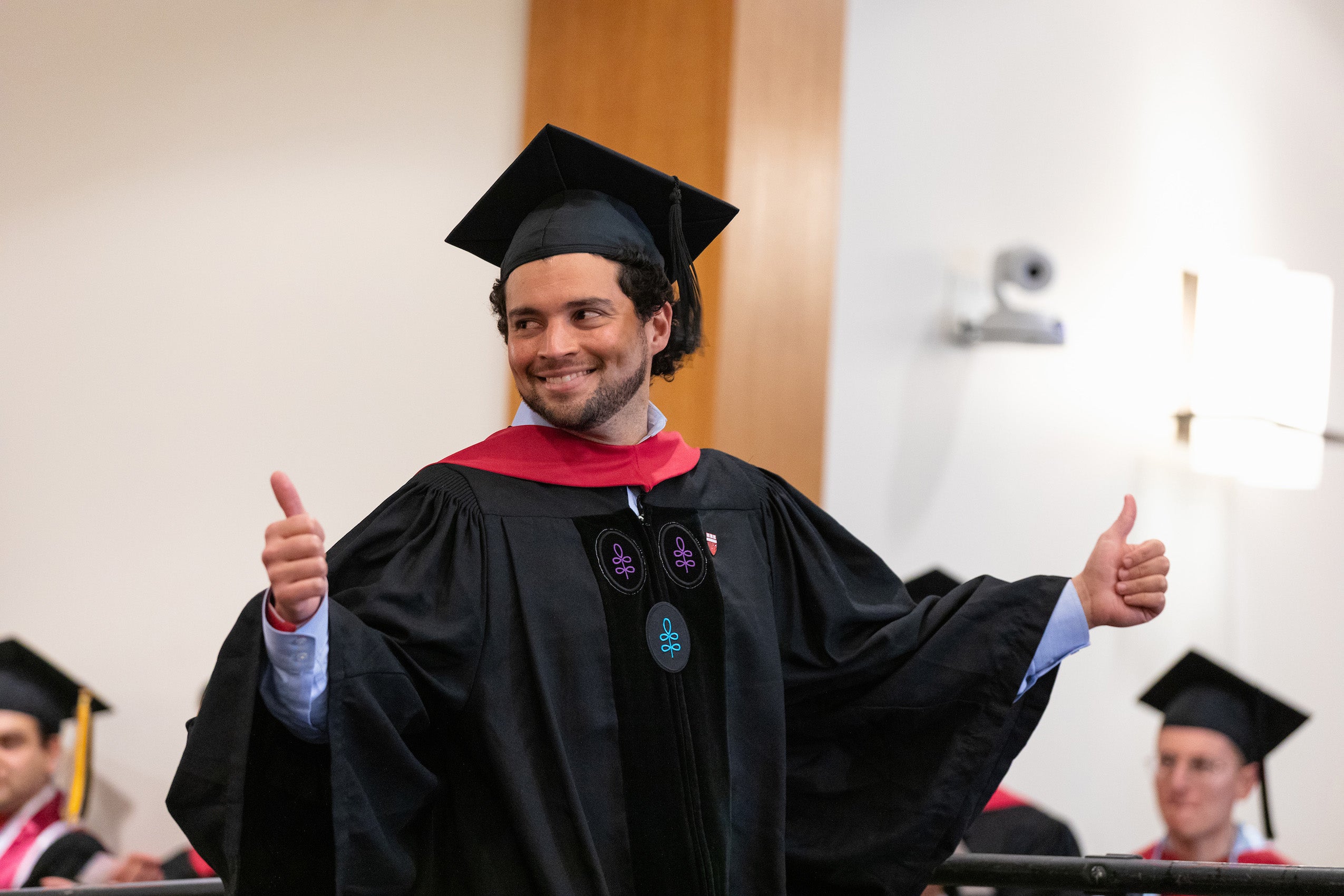 A man wearing a cap and gown gives a thumbs up as he gets on the stage to receive his diploma