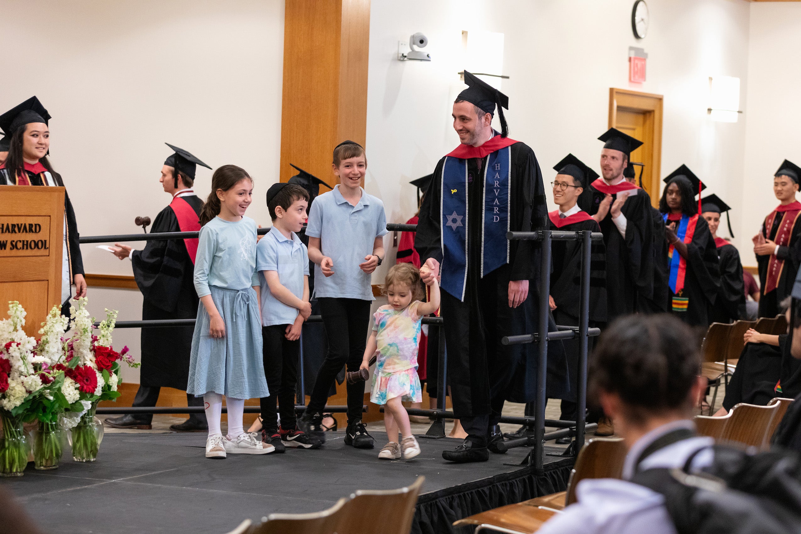 A man in cap and gown takes his four young children across the stage as he gets his diploma.