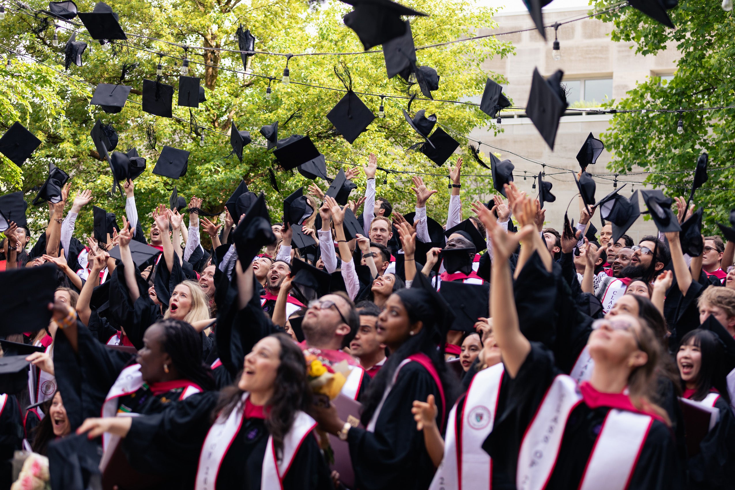 A large group of students in cap and gown throw their caps into the air
