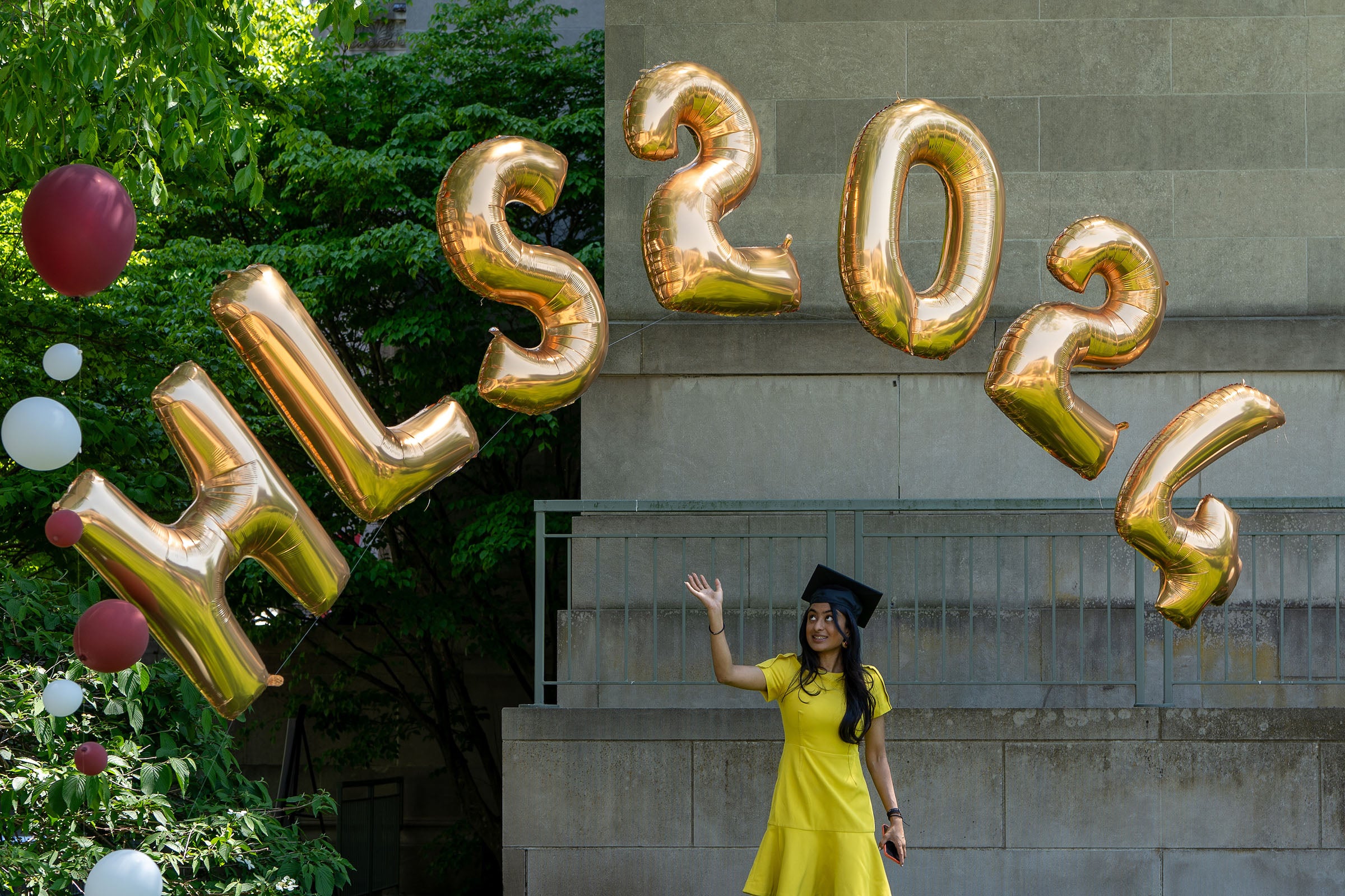 Graduate pointing to balloons that spell out HLS 2024.