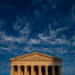 The front of the U.S. Supreme Court in daylight sits in the lower third of an image with dark blue and white clouds above