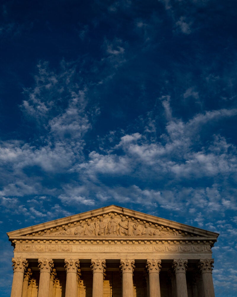 The front of the U.S. Supreme Court in daylight sits in the lower third of an image with dark blue and white clouds above