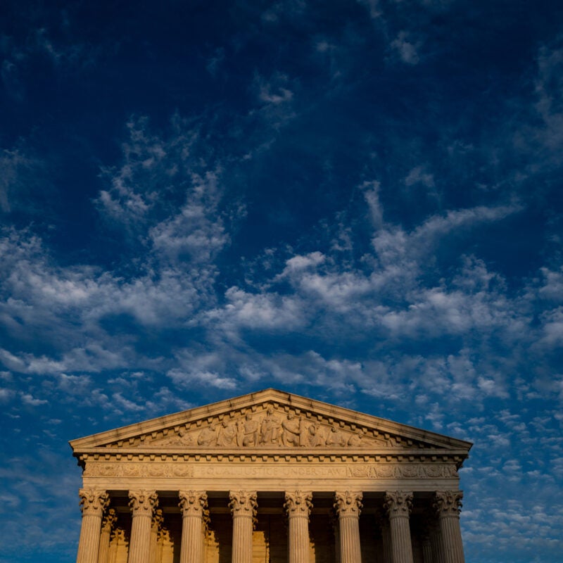 The front of the U.S. Supreme Court in daylight sits in the lower third of an image with dark blue and white clouds above