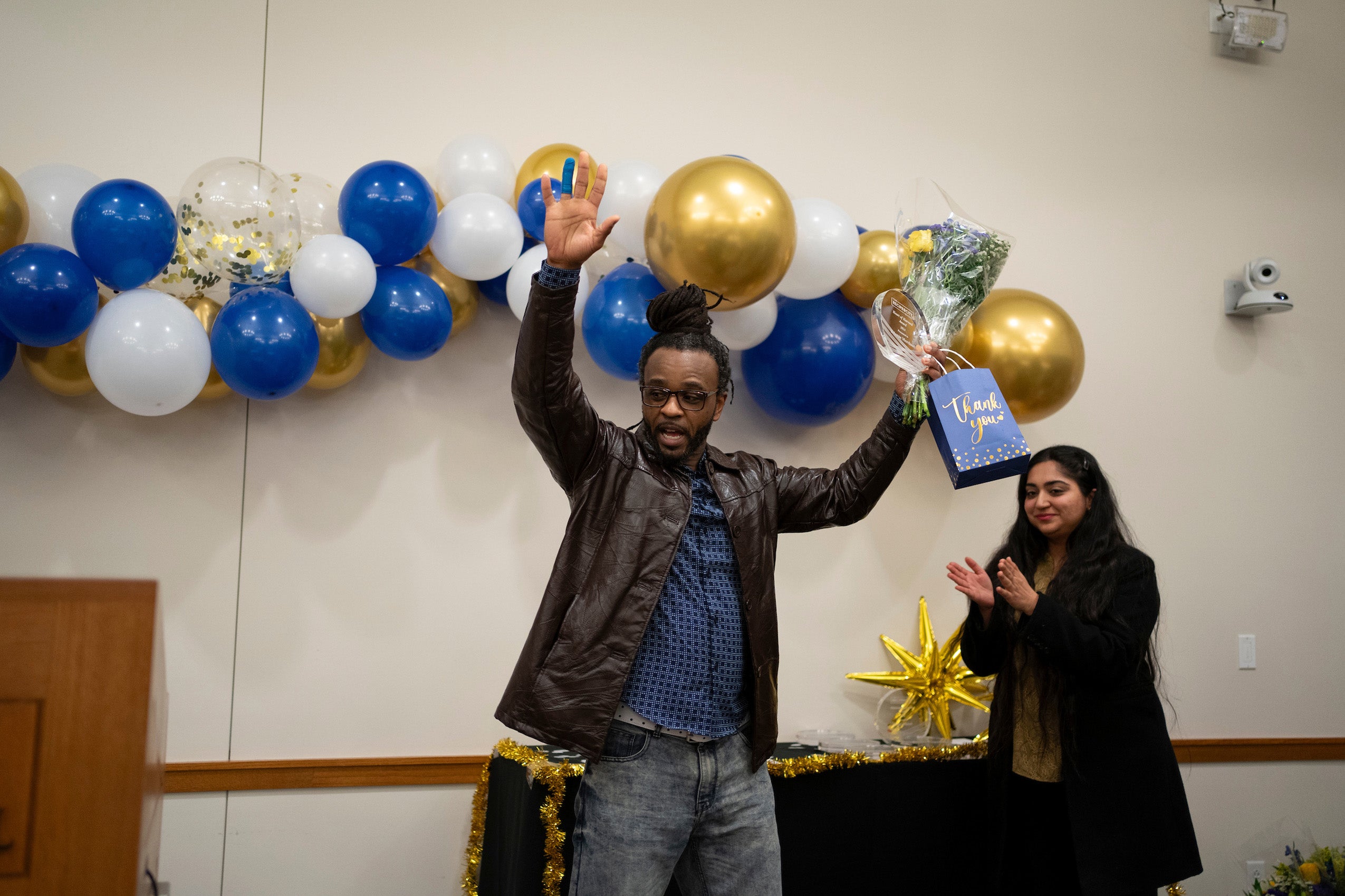 A man holds up a thank you bag and award as he is recognized.