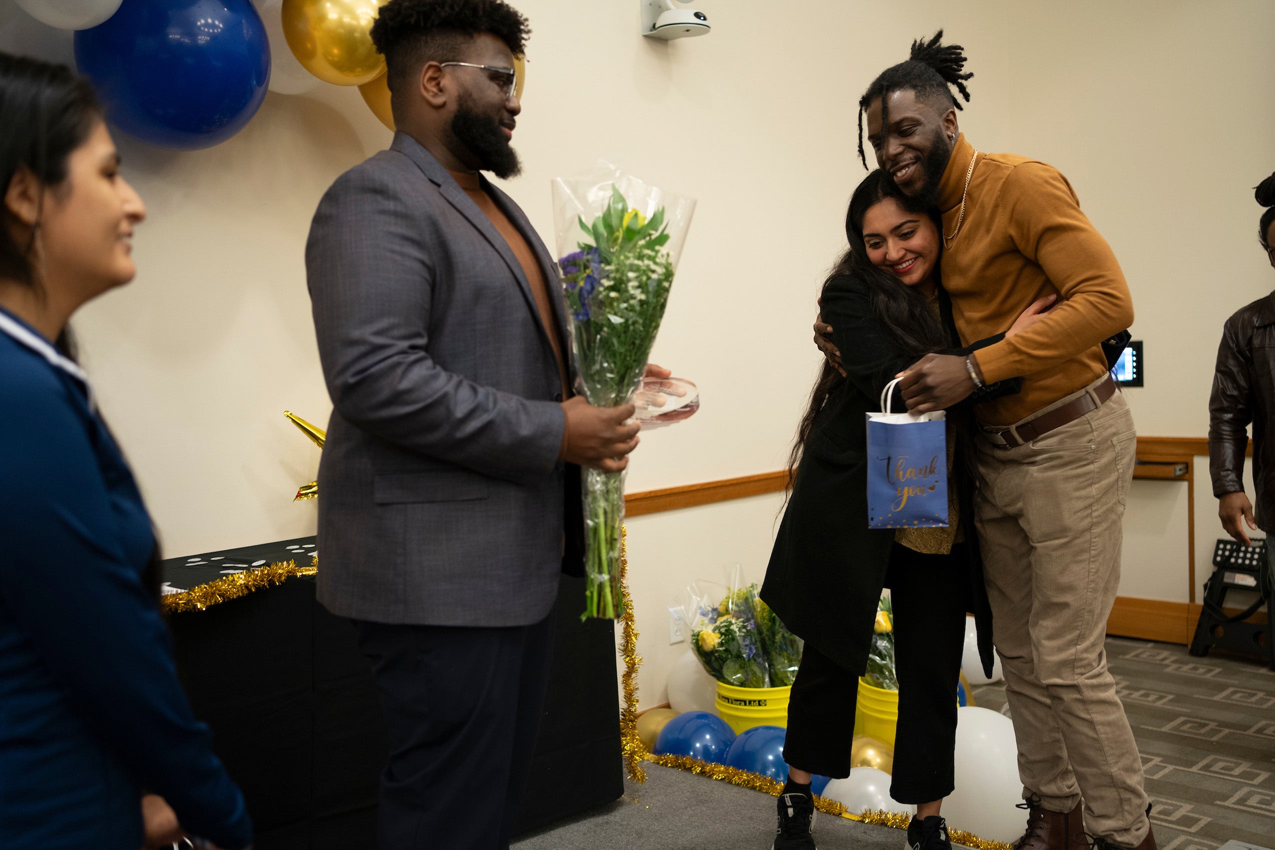 A woman hugs a man after receiving an honor as another person looks on with some flowers.