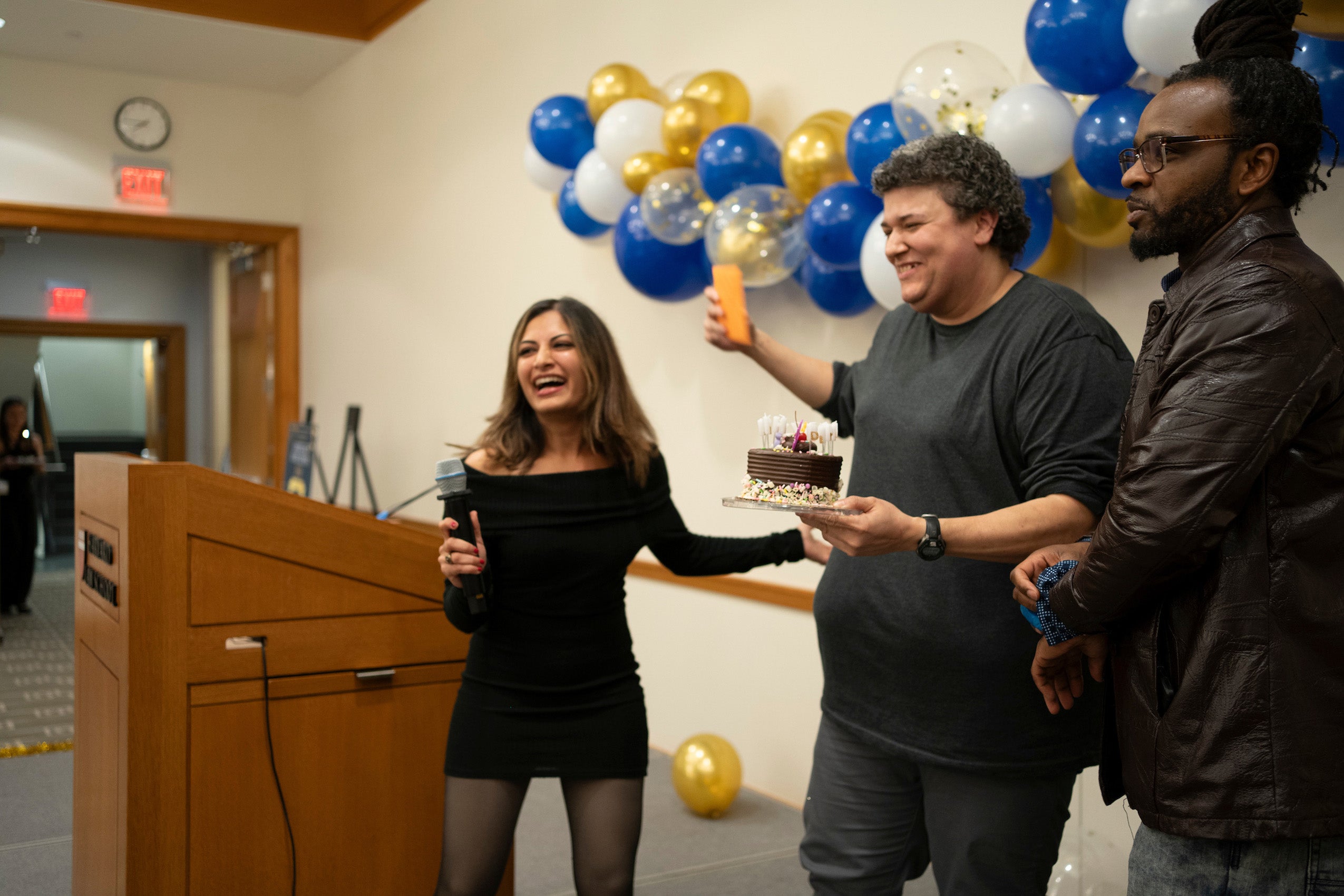 A woman gives another woman a cake at the front of the room at an event.