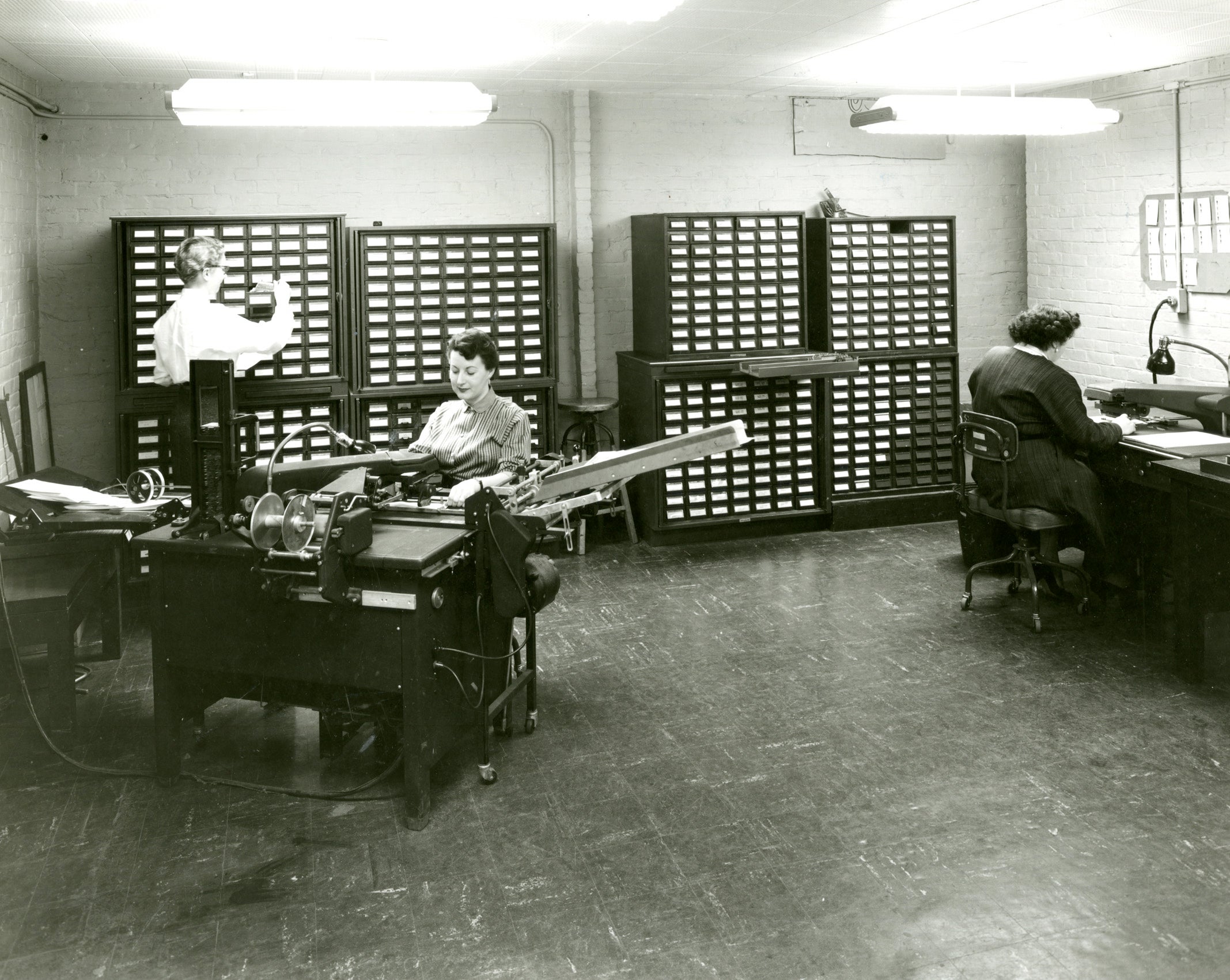 A room with walls of cabinets with small drawers and a large machine.