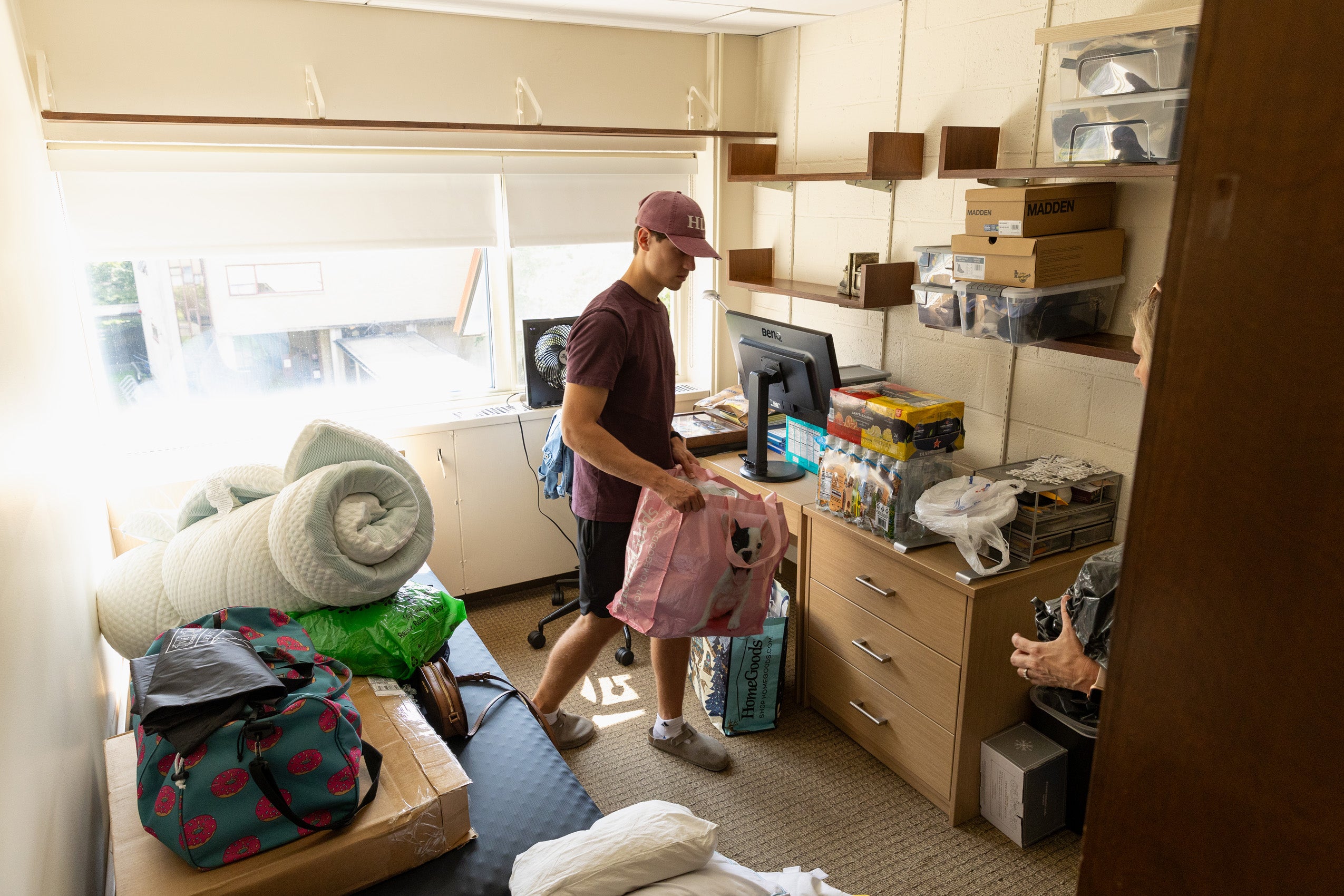 A man holds a bag in a dorm room.