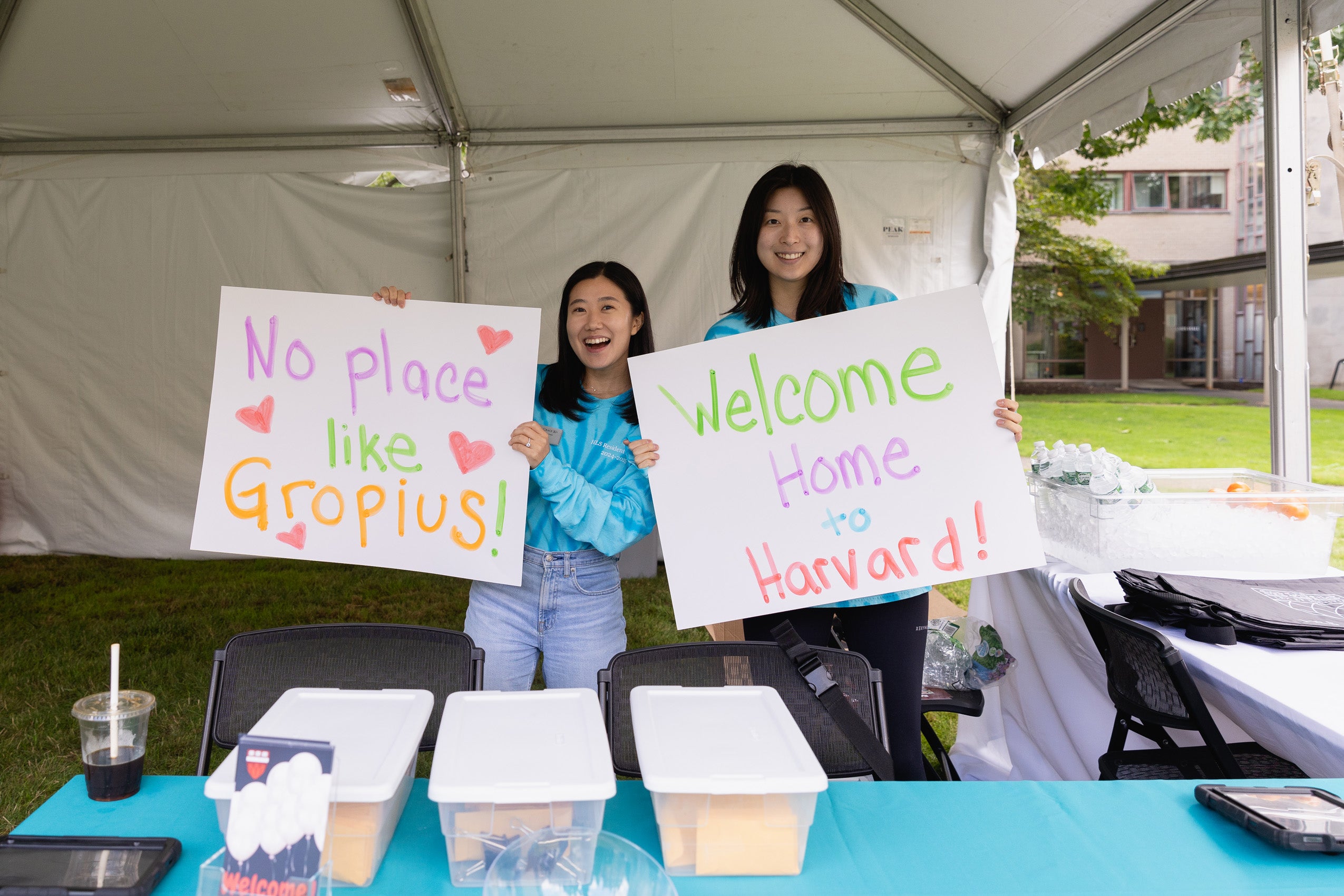 Two students under a white tent on campus during move in hold signs that say