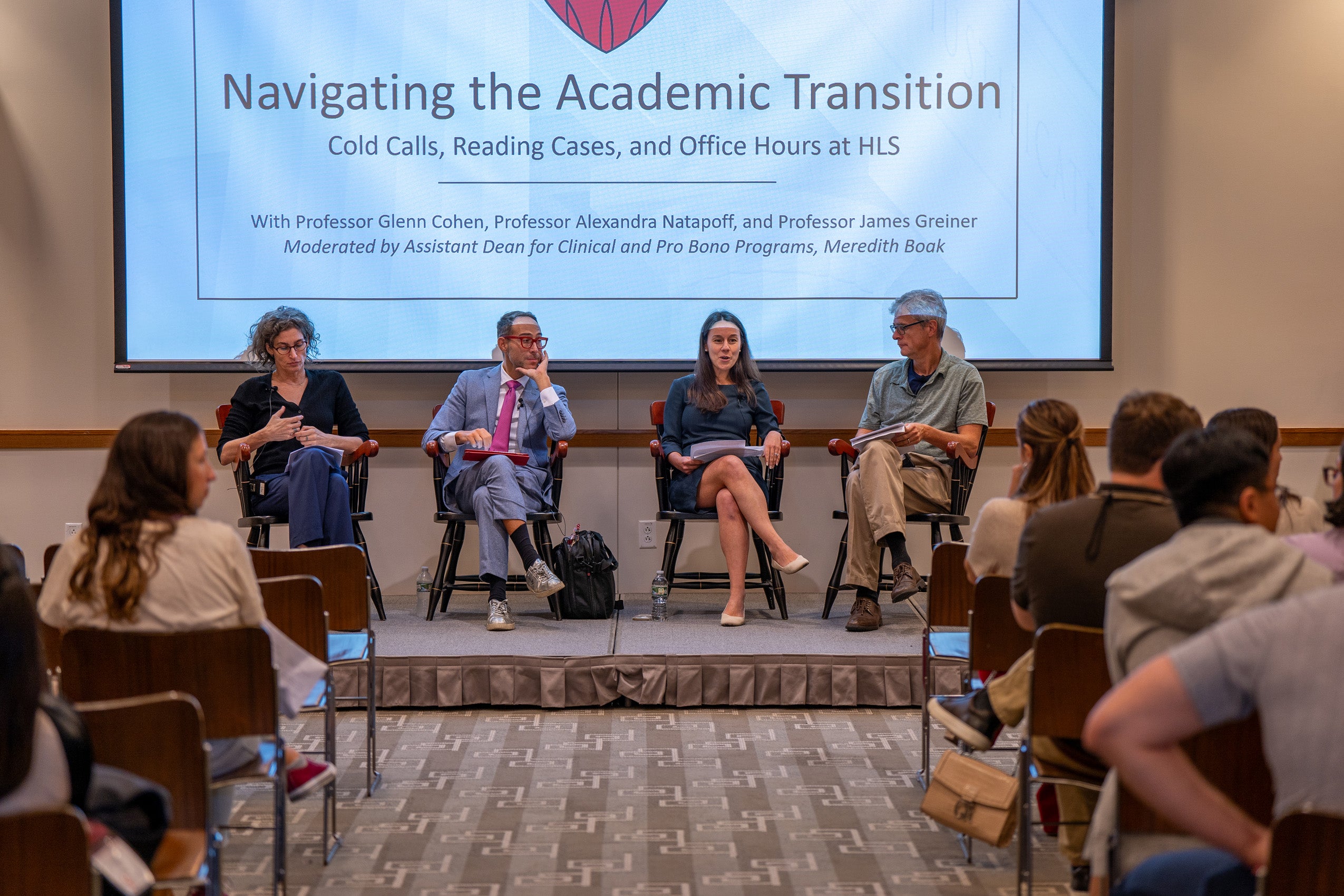 A panel of 4 people speaking to an audience in front of a large sign that says