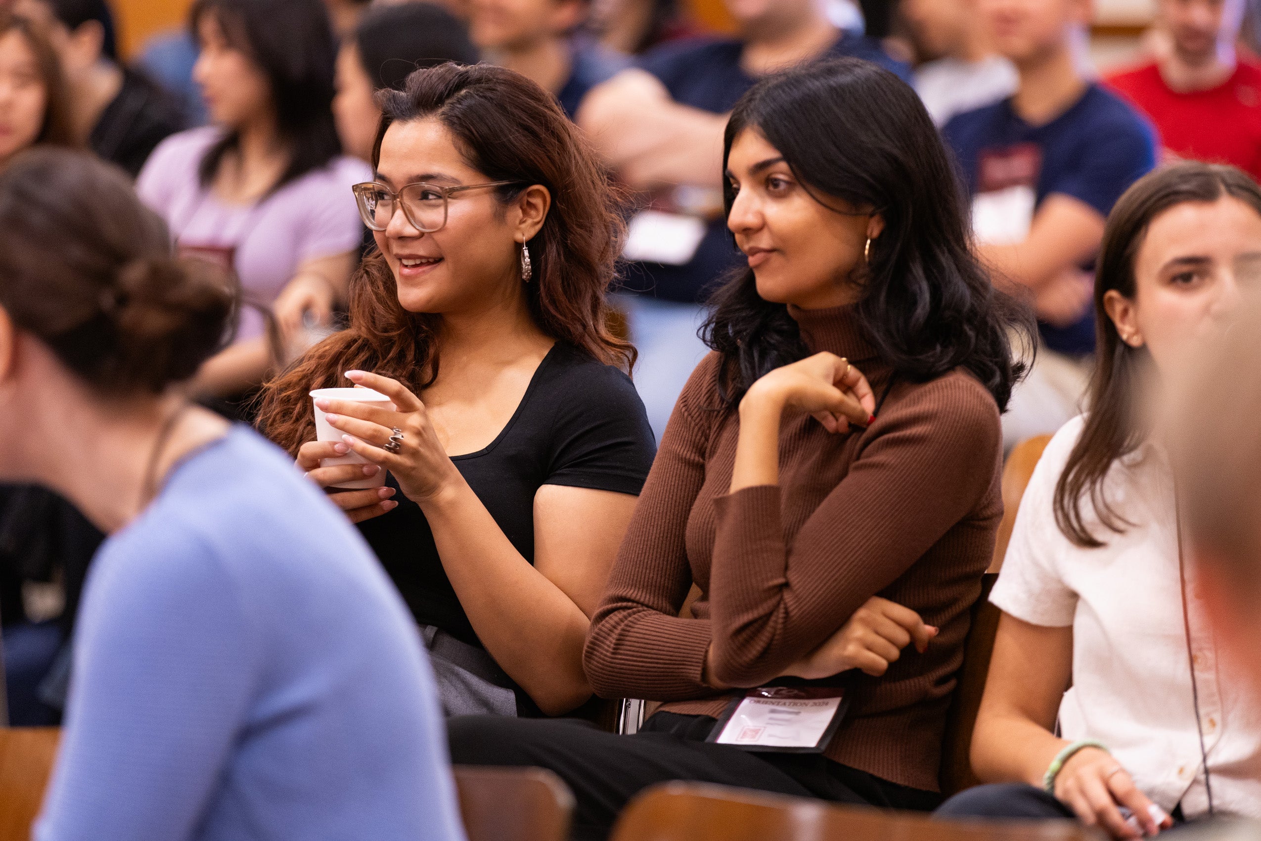 Two women sitting in a row of students at an orientation event.