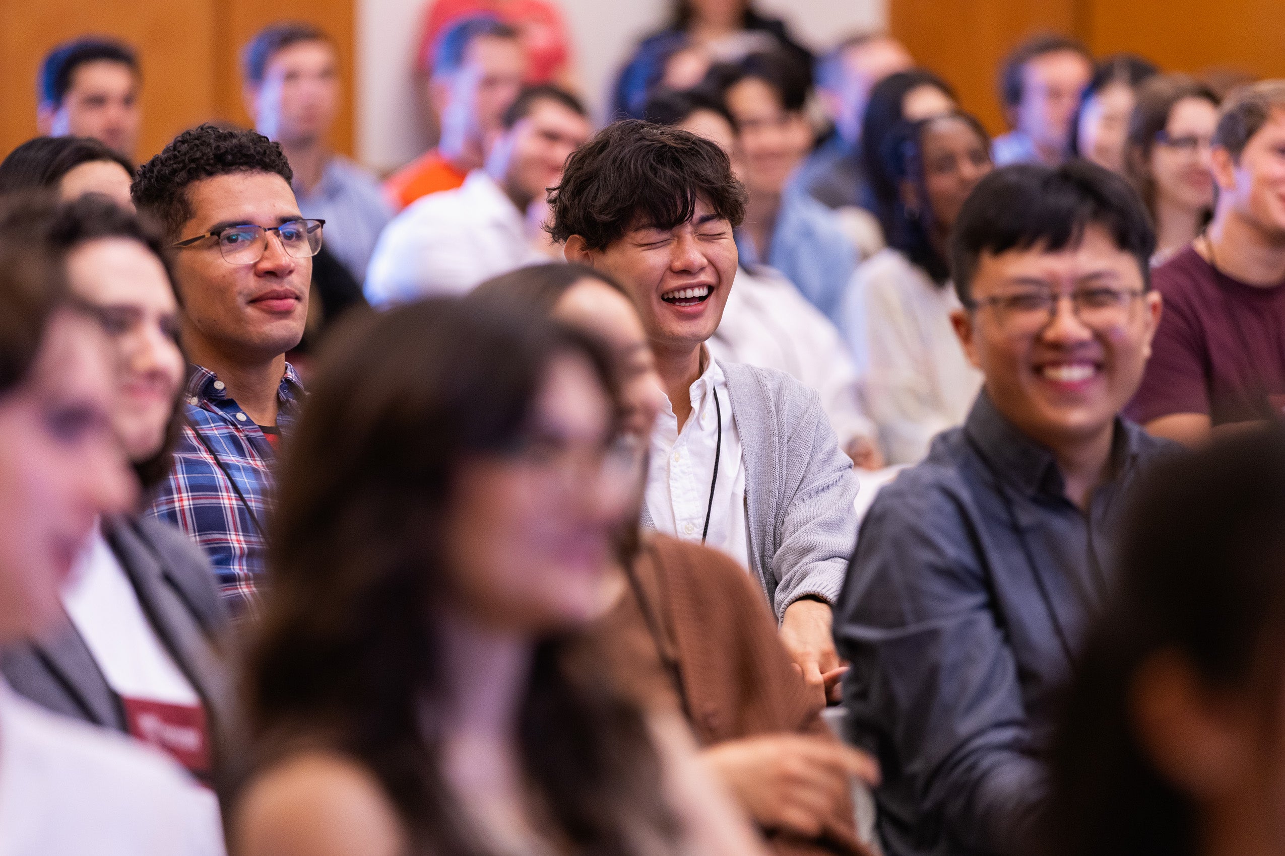 A man in a row of students at an event laughs as he listens to remarks.