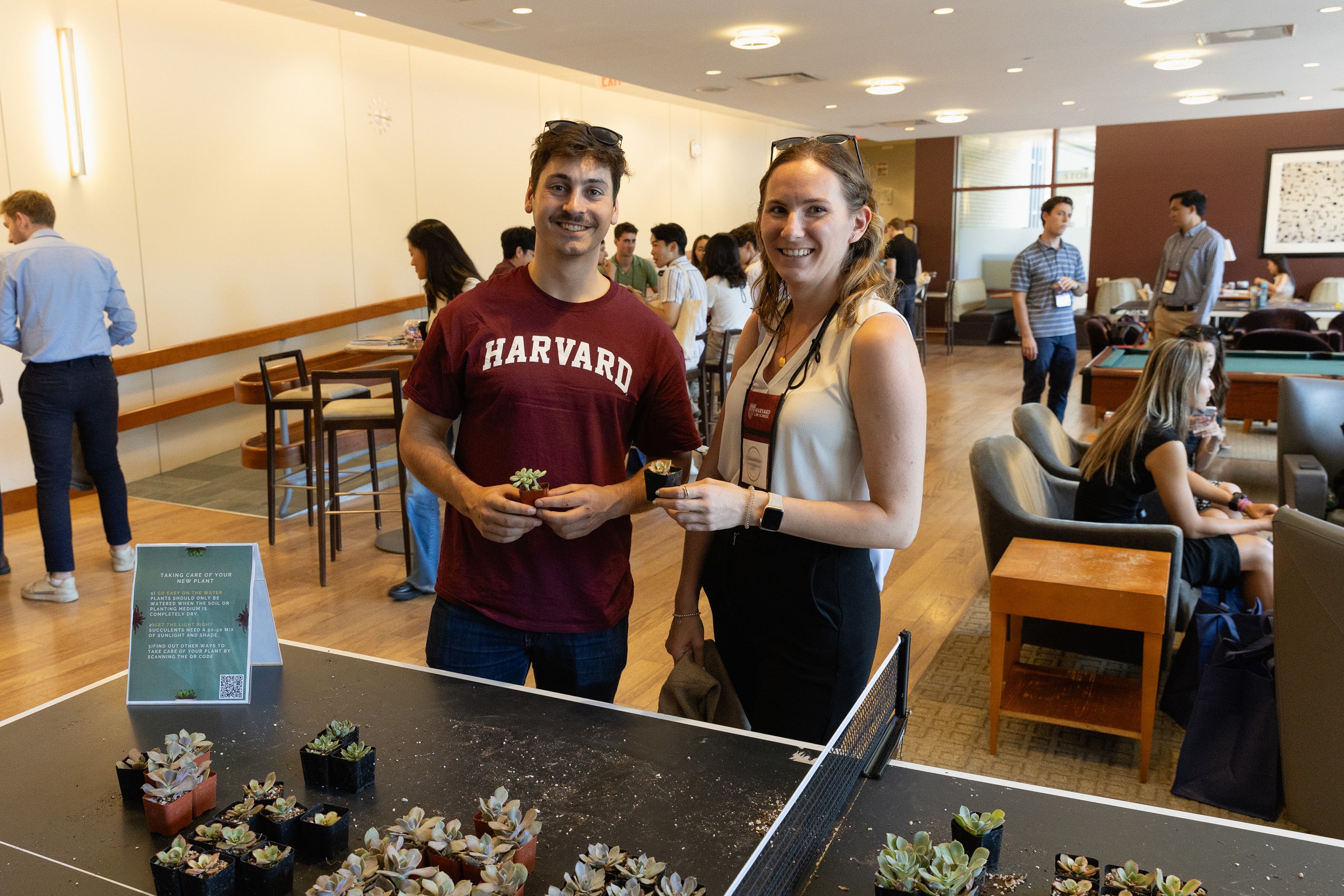 A man an a woman hold a small plant that they picked up from a table during orientation.