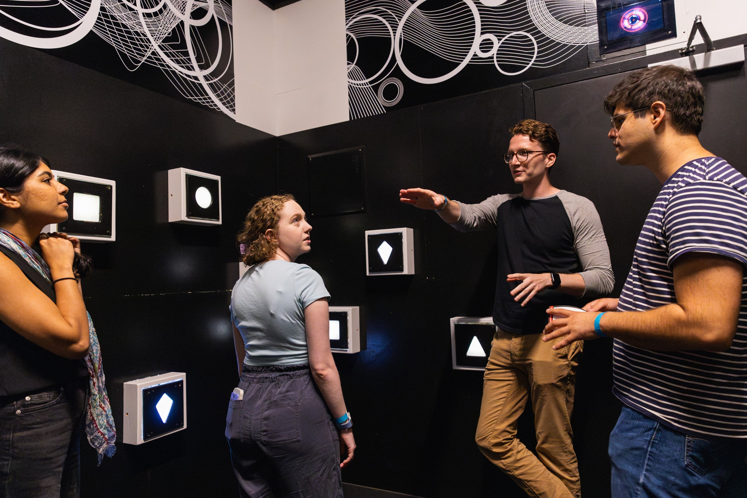 Four people in a black room with framed squares and circles on the walls.