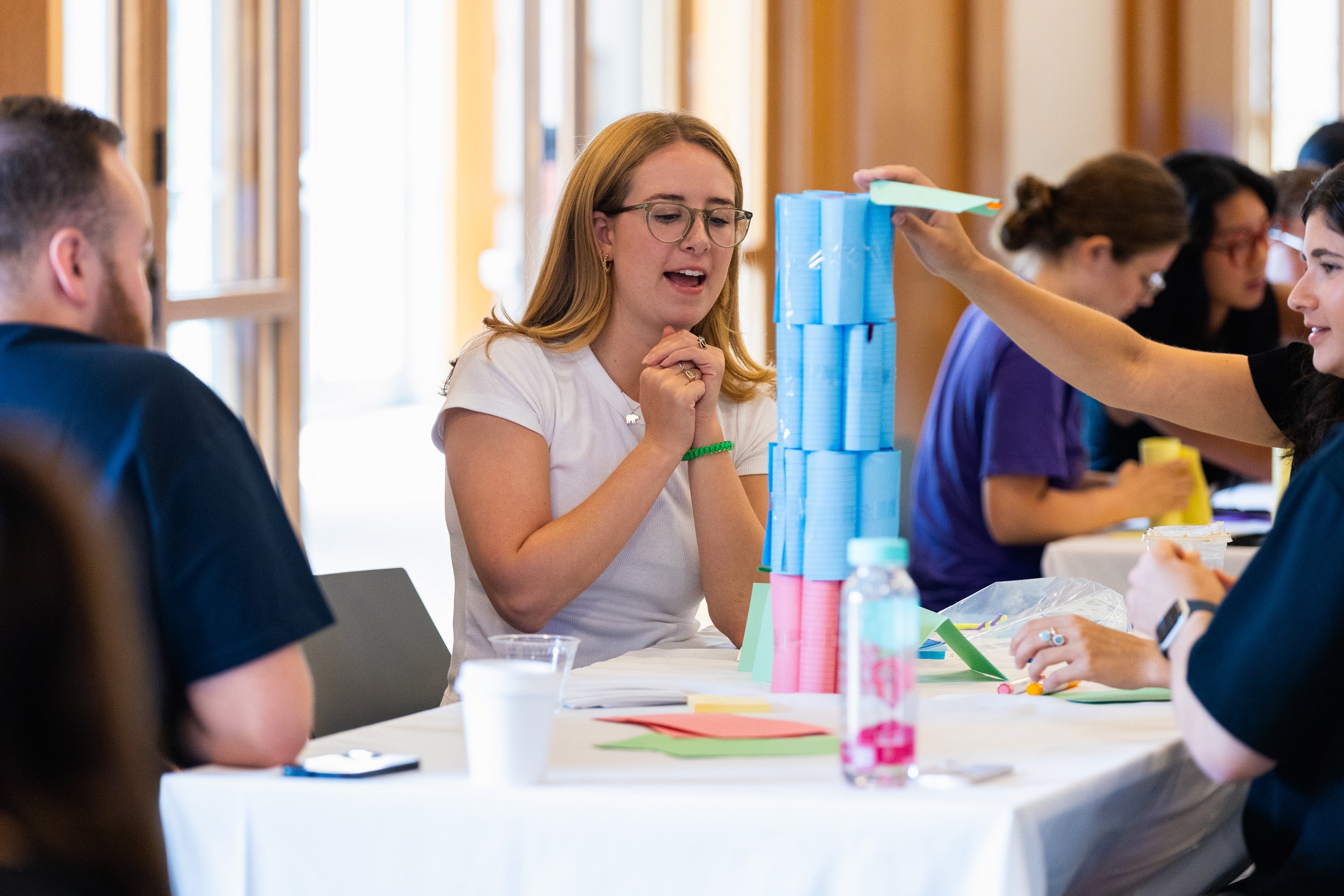 Students at a table build a tall paper structure during orientation event.