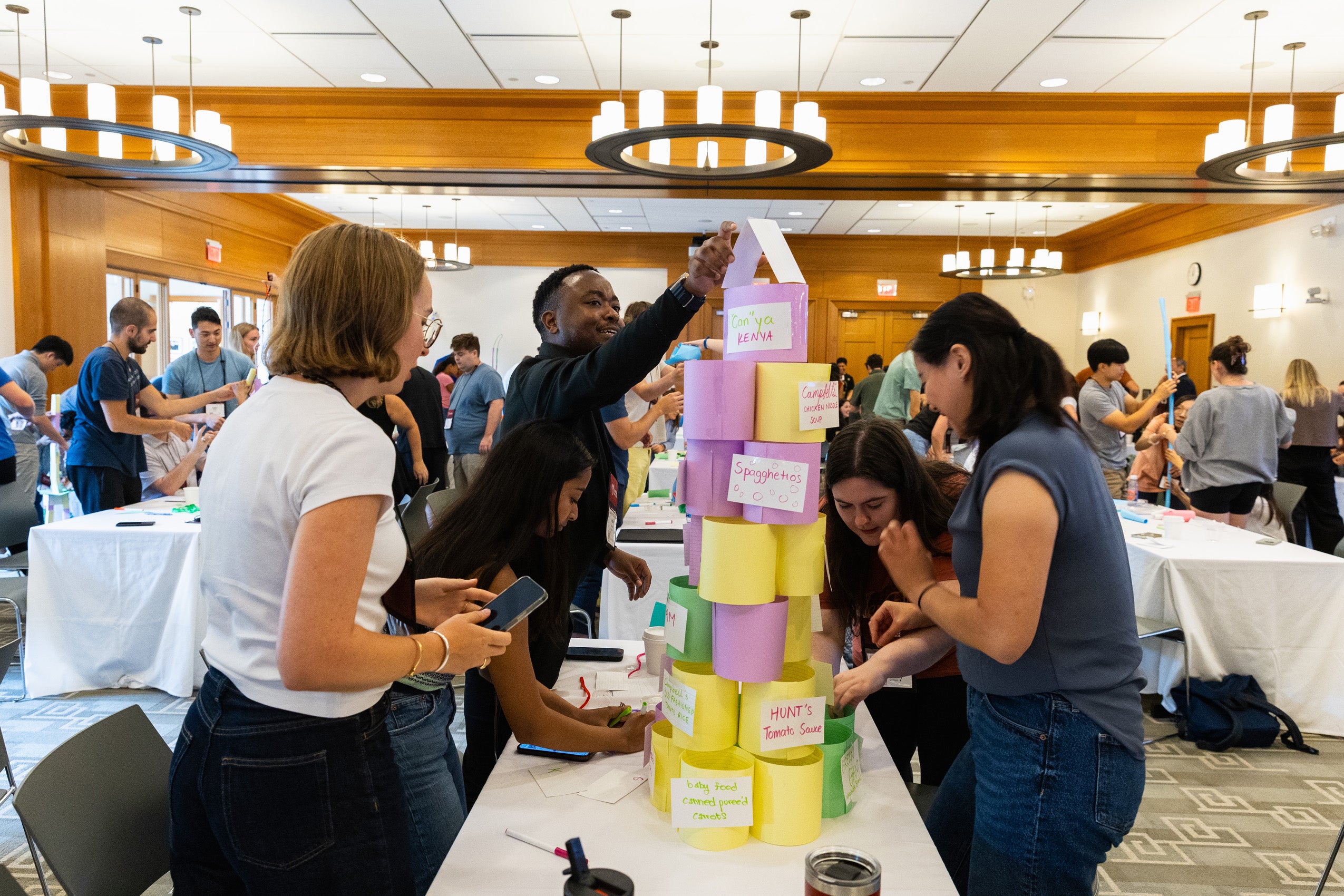 Several students at a table build a tall paper structure during orientation event.