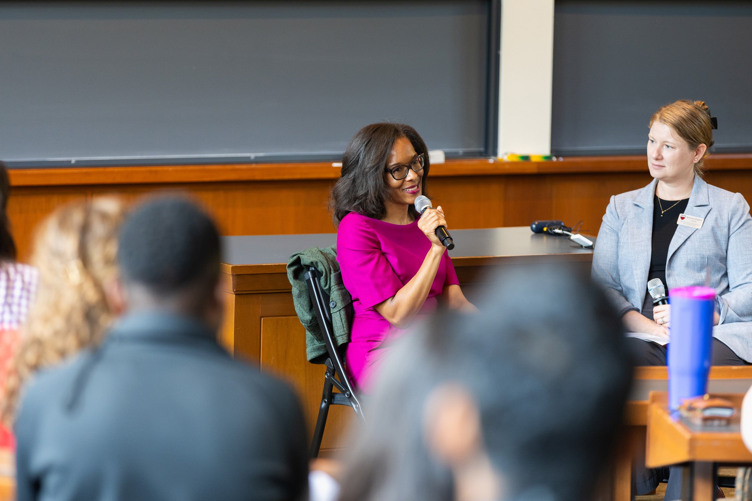 A woman holding a microphone speaks at the front of a classroom