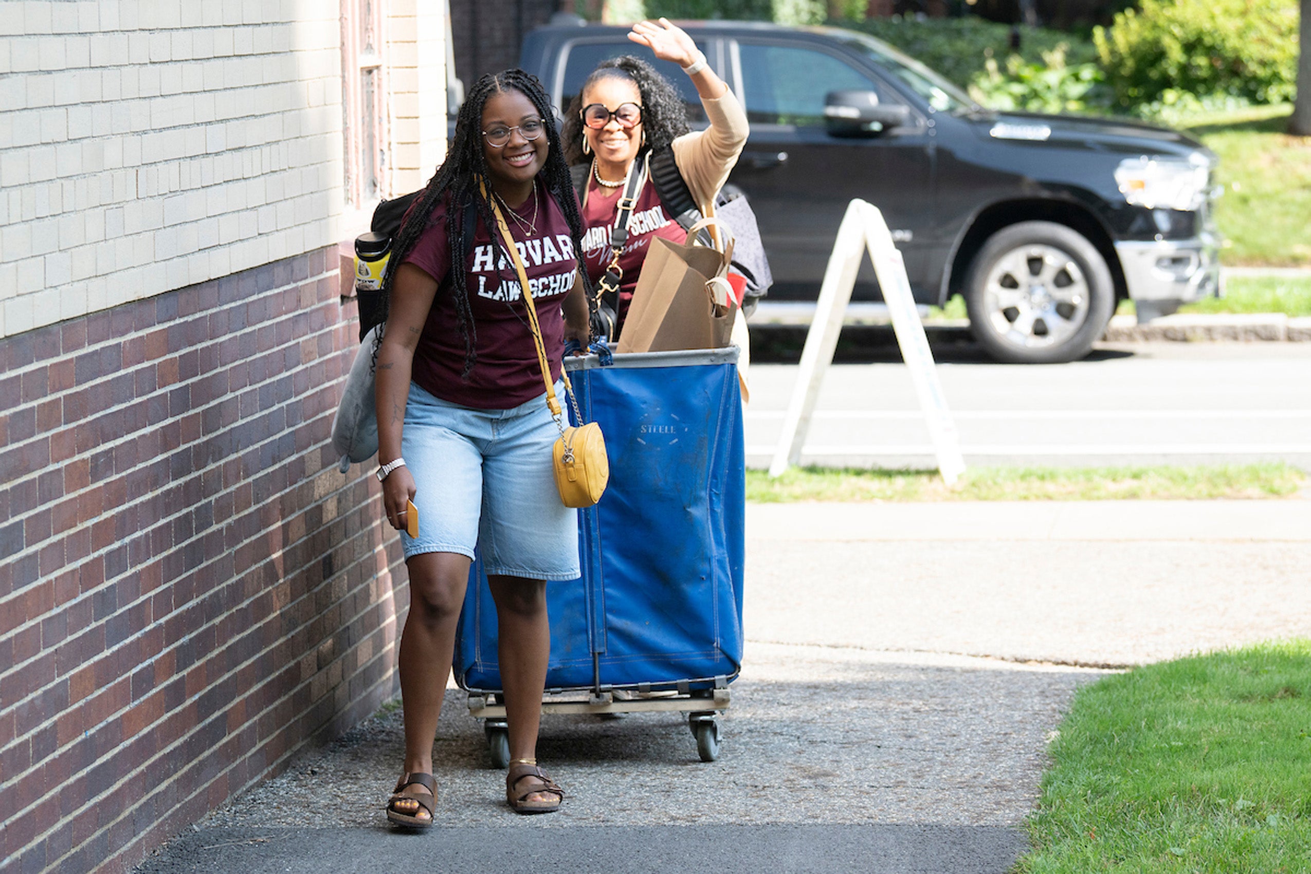 Two student wave as they lug a large container of items towards their room on move in day.