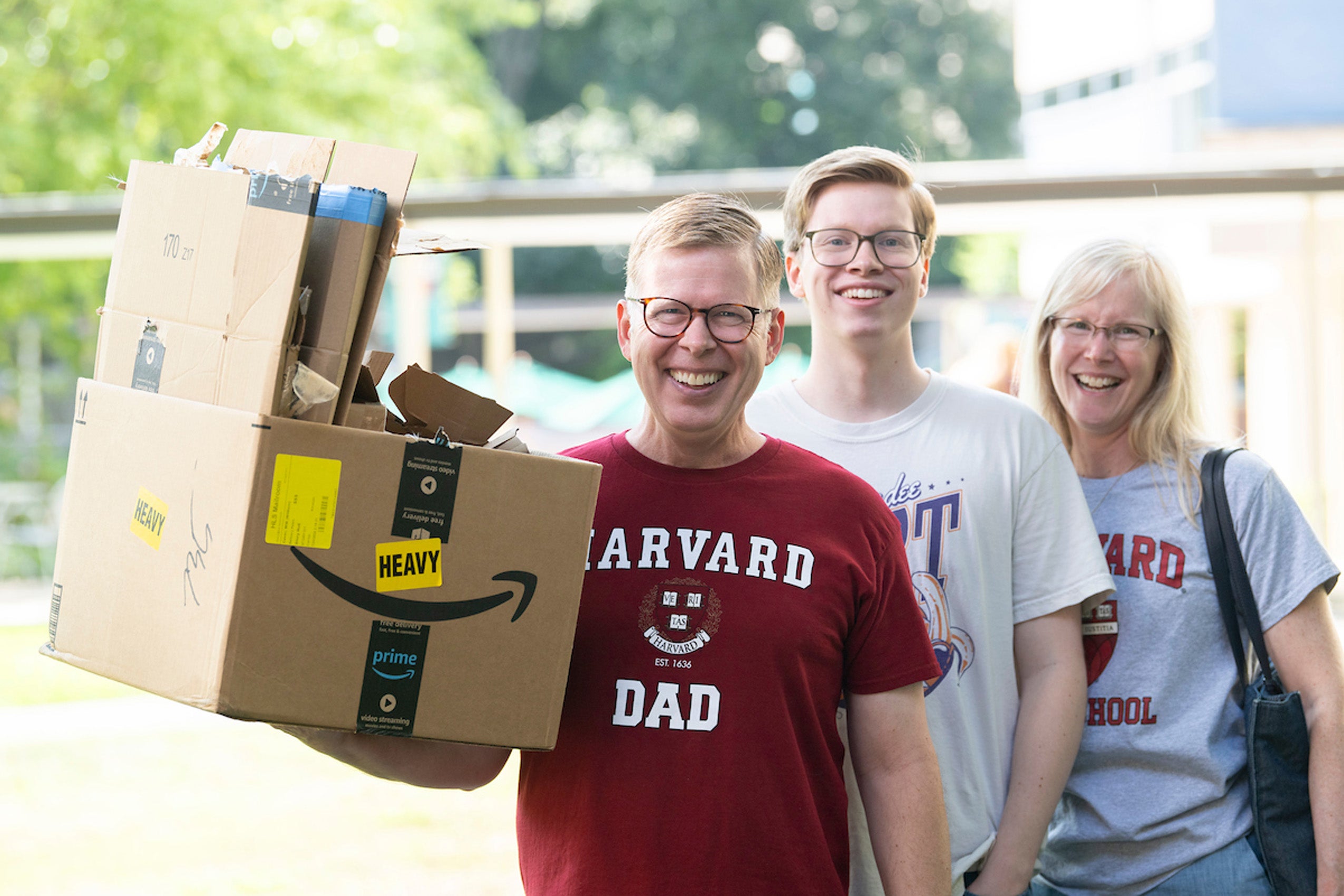 A man and woman wearing Harvard Law T-shirts with their son pose for a photo holding a pile of boxes on move in day.