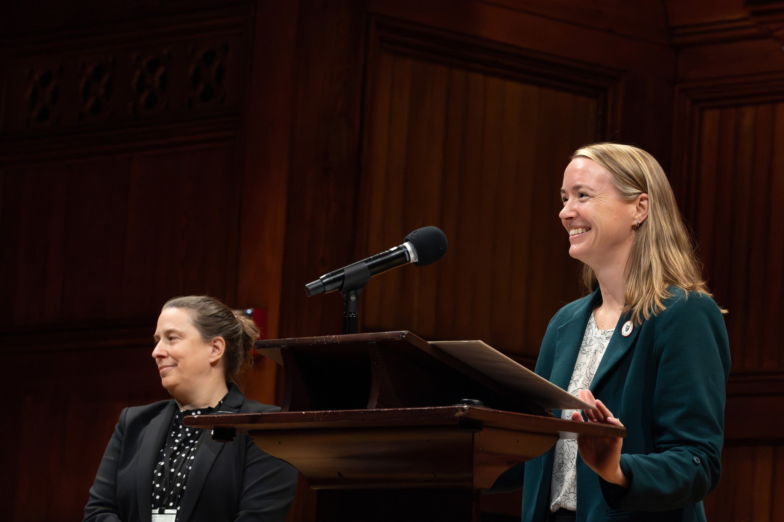 A woman addresses an audience from a podium and another women stands nearby during an orientation event in Sanders.