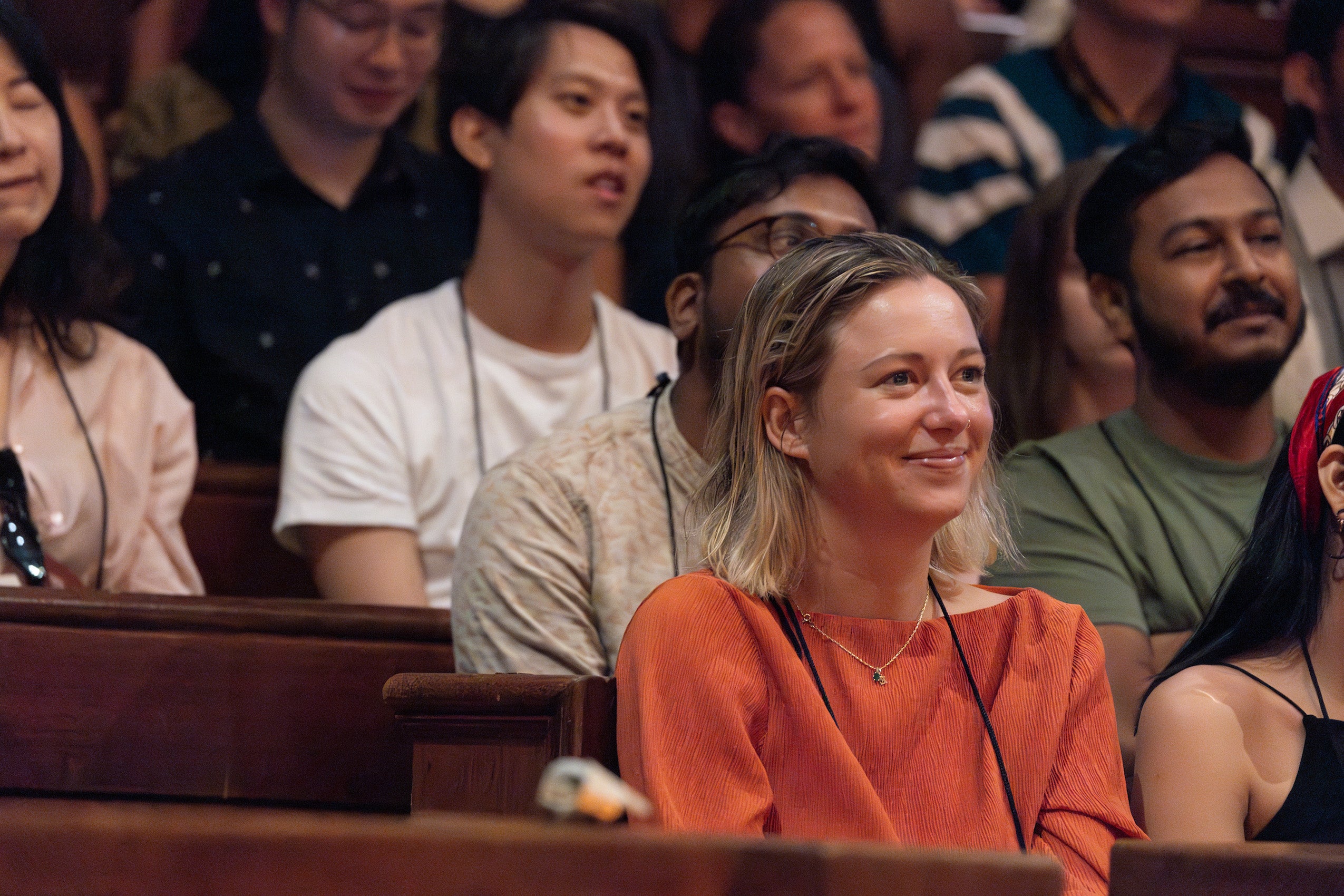 A close up of a smiling student in a crowd as she sits watching remarks in Sanders during orientation.