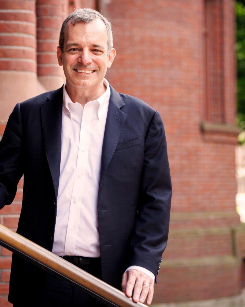 A portrait of Dean Manning in front of a red brick building in Harvard Yard.