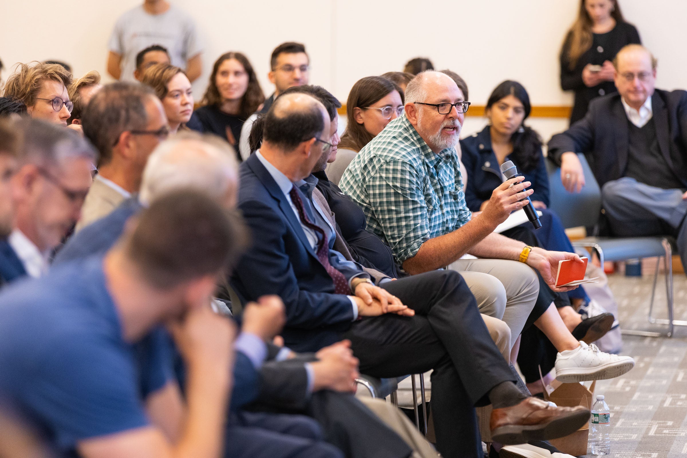 A man speaks into a microphone from his seat in an audience.