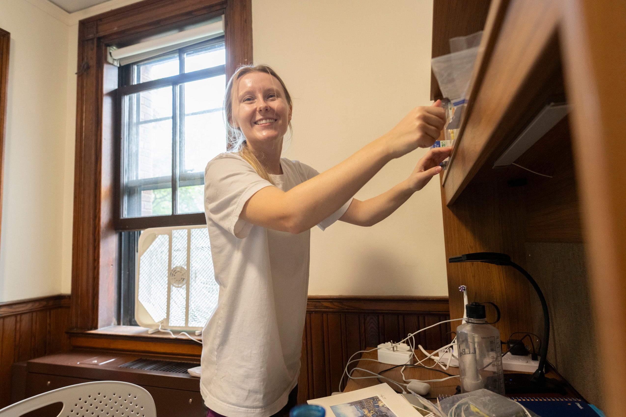 A woman looks up as she is unpacking items on her wooden desk.