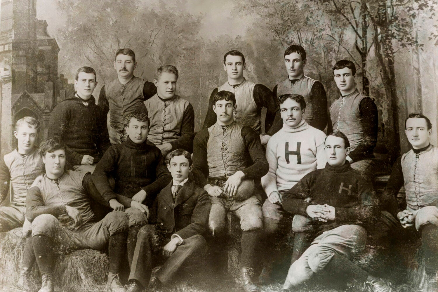 A formal group shot of men some in a sports uniform. One man is waring a white shirt with a large 