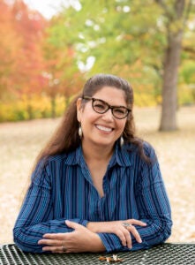 A portrait of a women sitting outside leaning on a table.