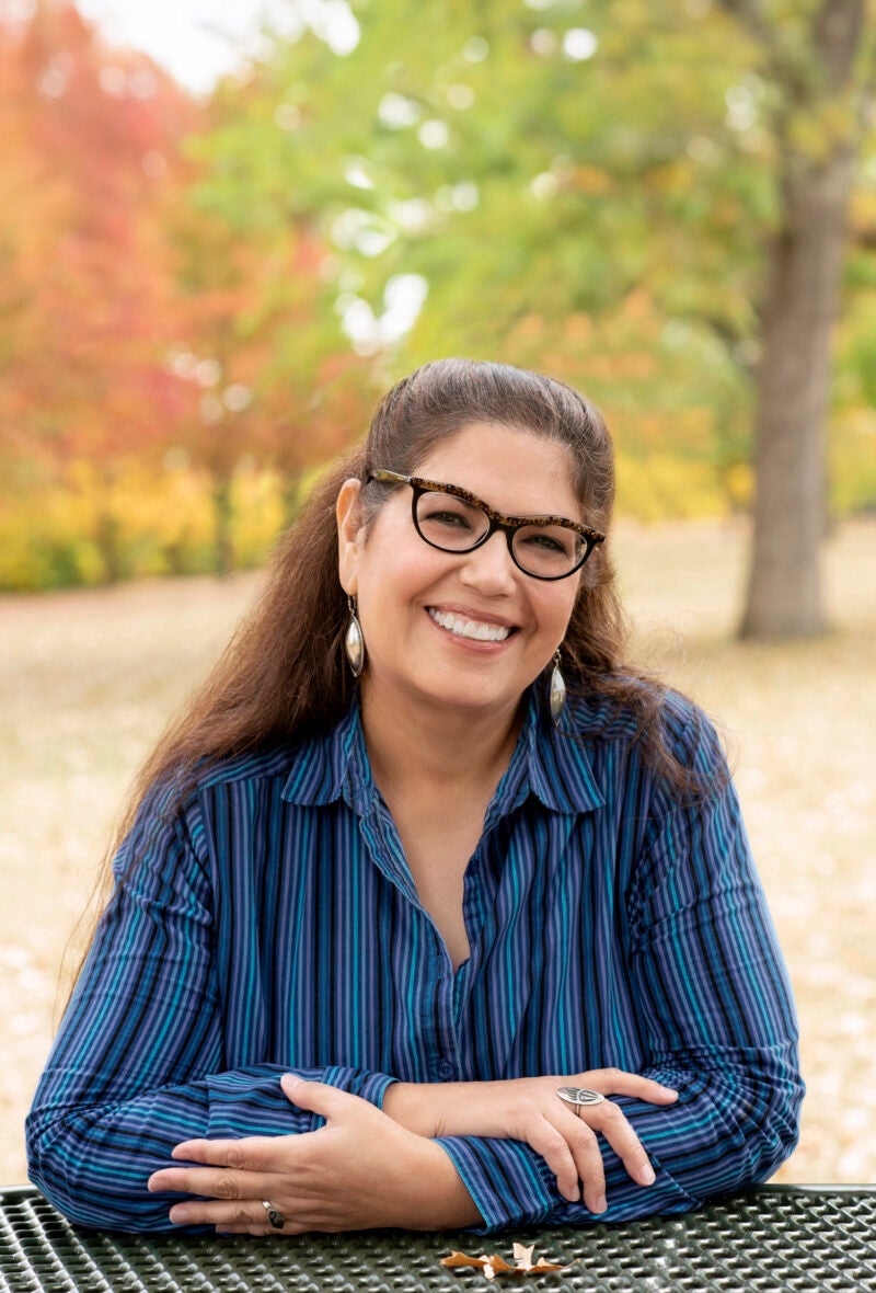 A portrait of a women sitting outside leaning on a table.
