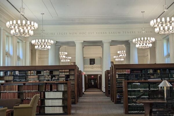 An expansive room with Greek Doric columns, tall ceilings, bookcases, and chandeliers.