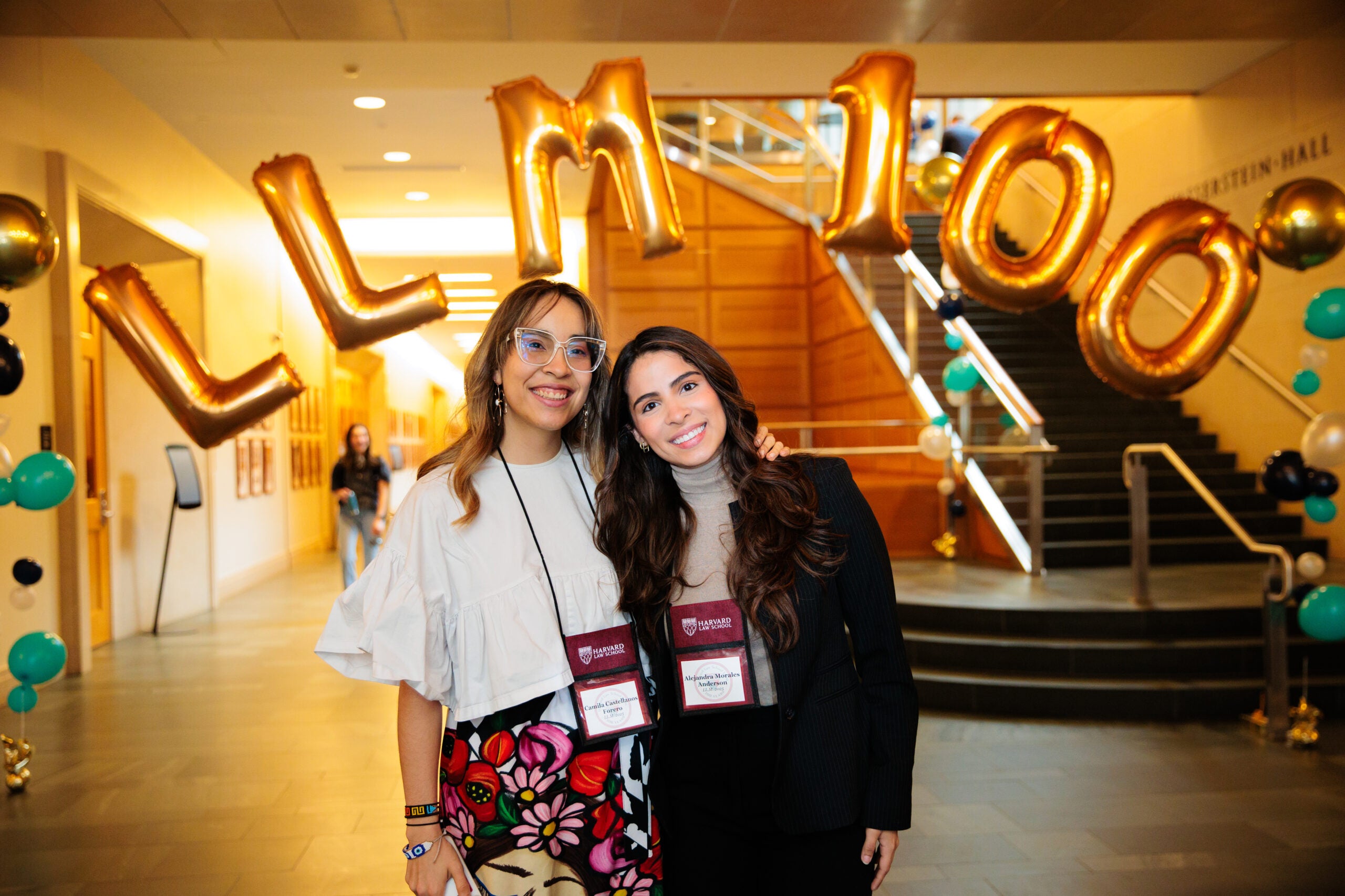 Two people stand in the corridor of a building with the gold balloons spelling out LL.M. 100 behind them. LL.M.