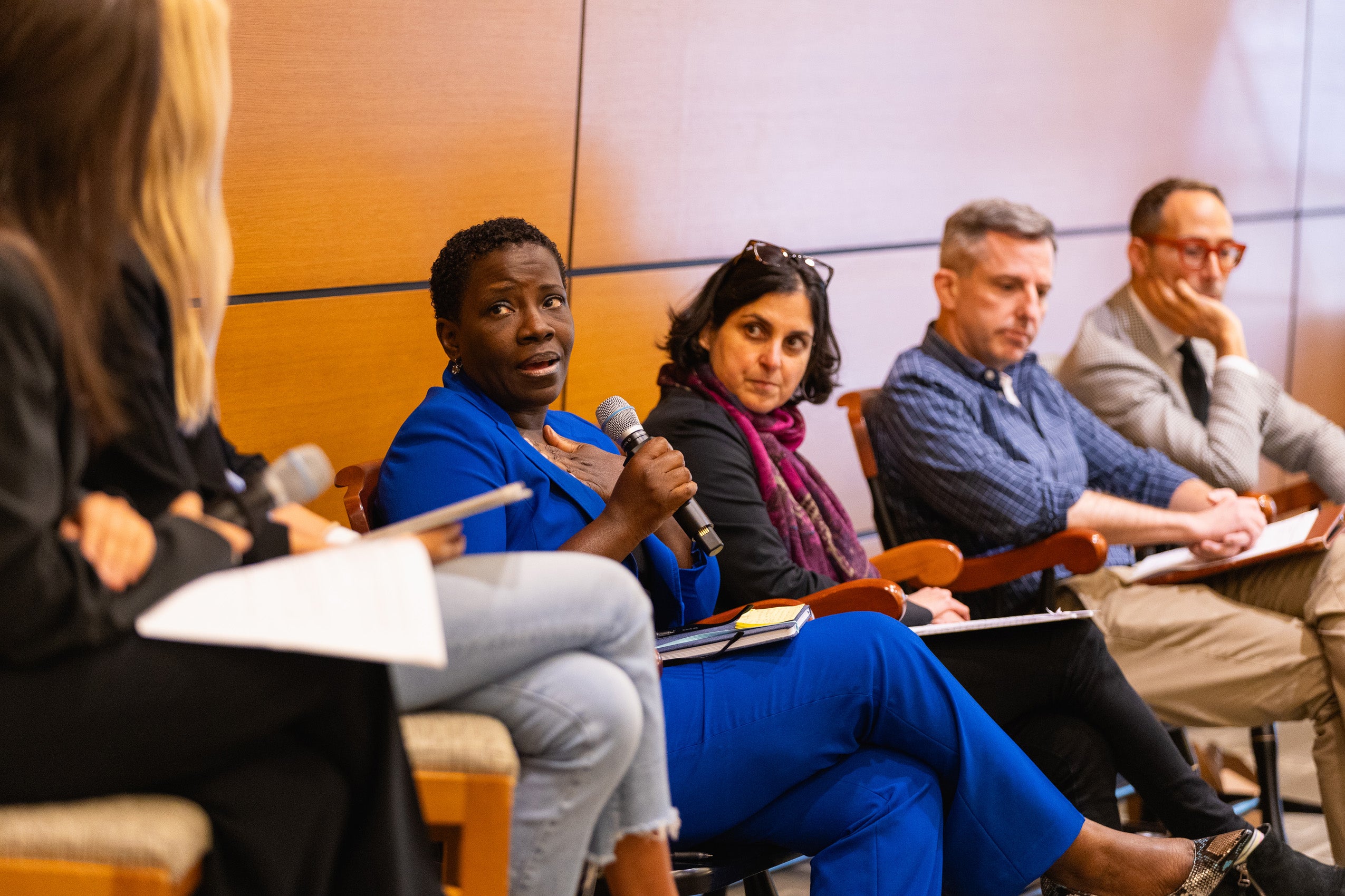 A woman holding a microphone sitting on a panel with three others.