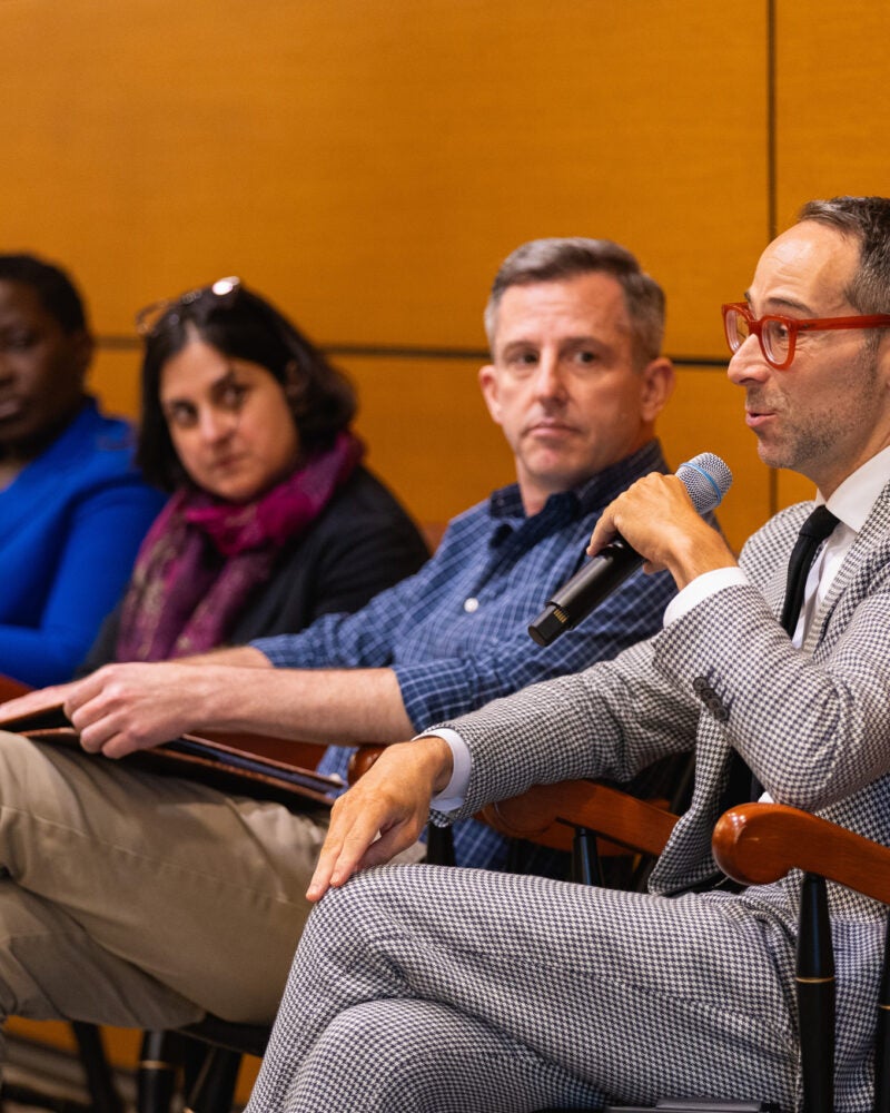 A close up of a man holding a microphone as he is speaking on a panel