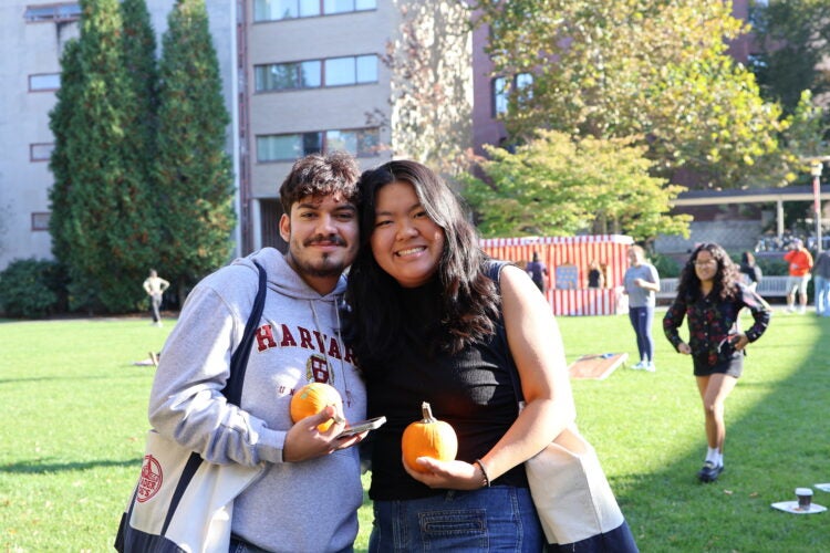 two students standing together holding pumpkins