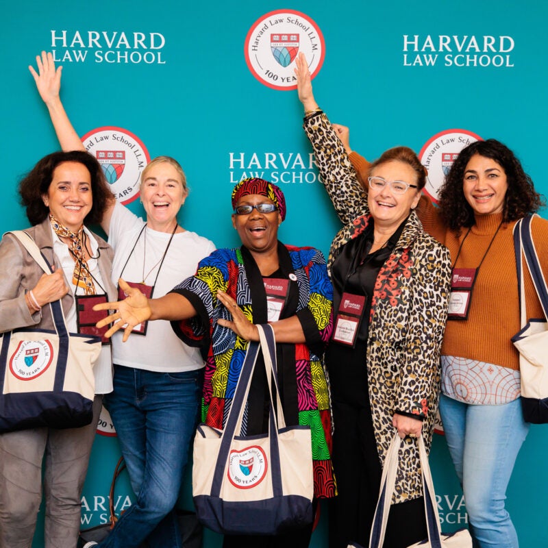 A group of women stand in front of a a teal backdrop posing for a photo at a celebration
