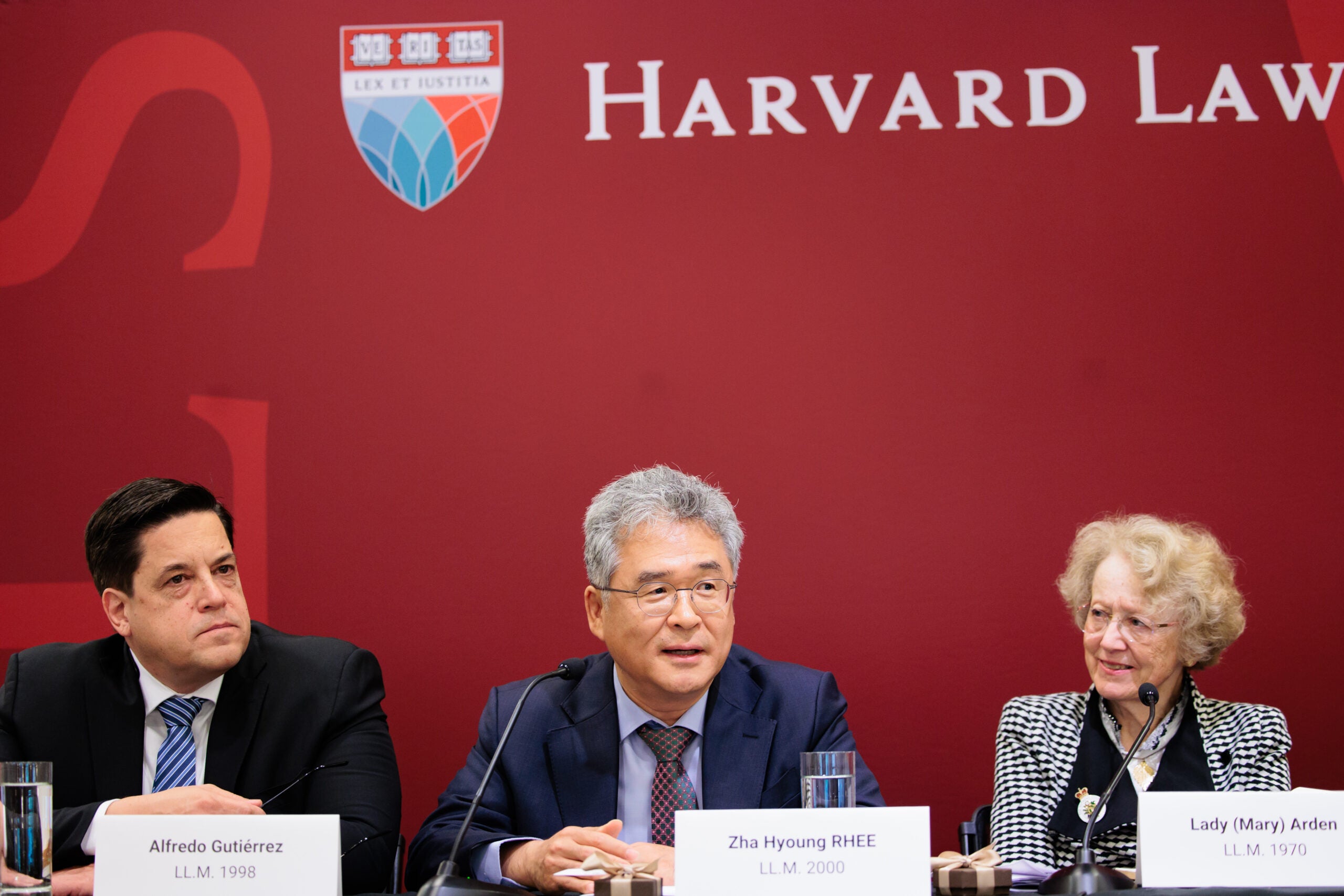 Three people sitting on a panel in front of a crimson background.